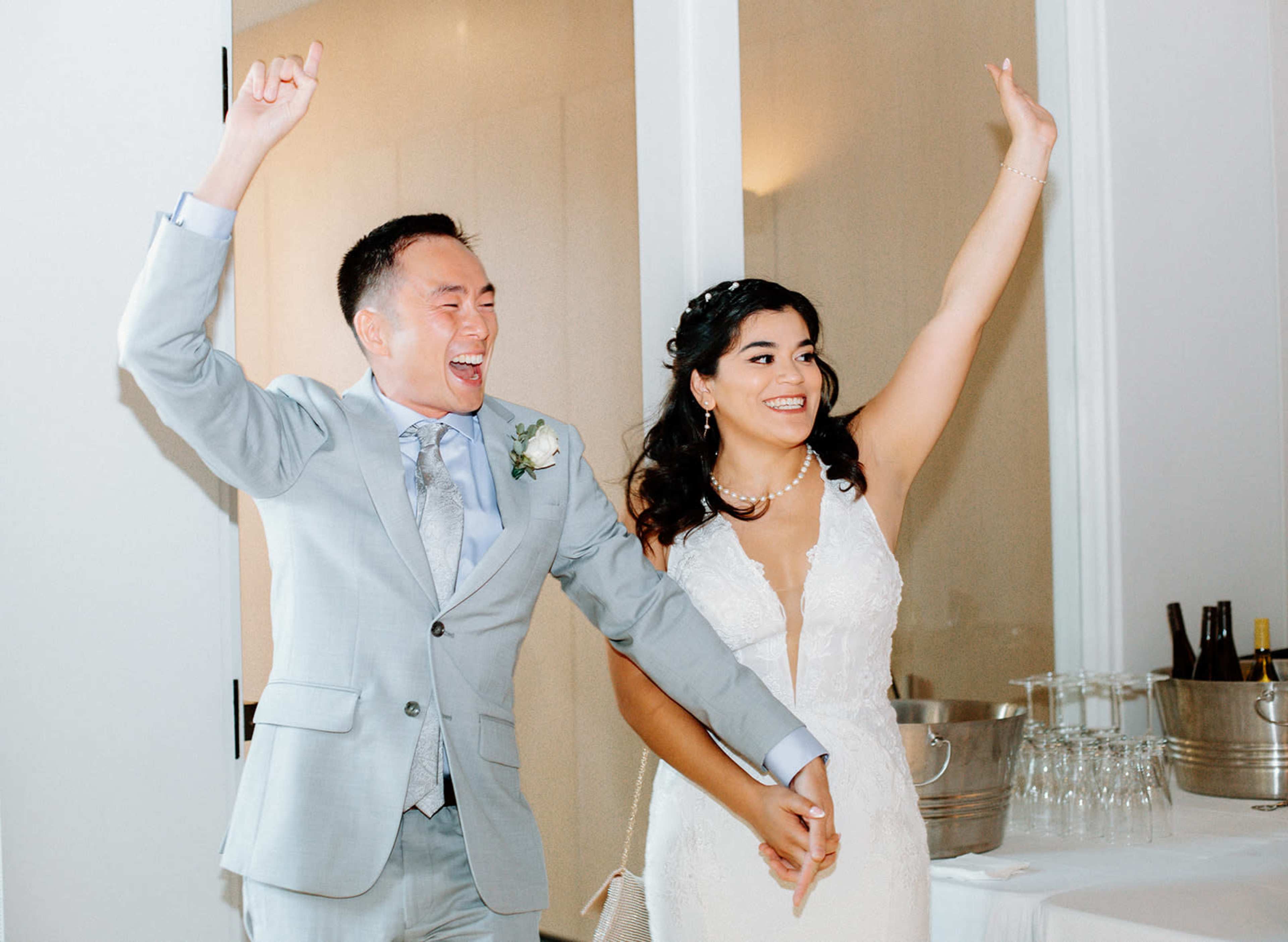 A man and a woman celebrate by raising their arms in a joyful gesture while holding hands at a reception.