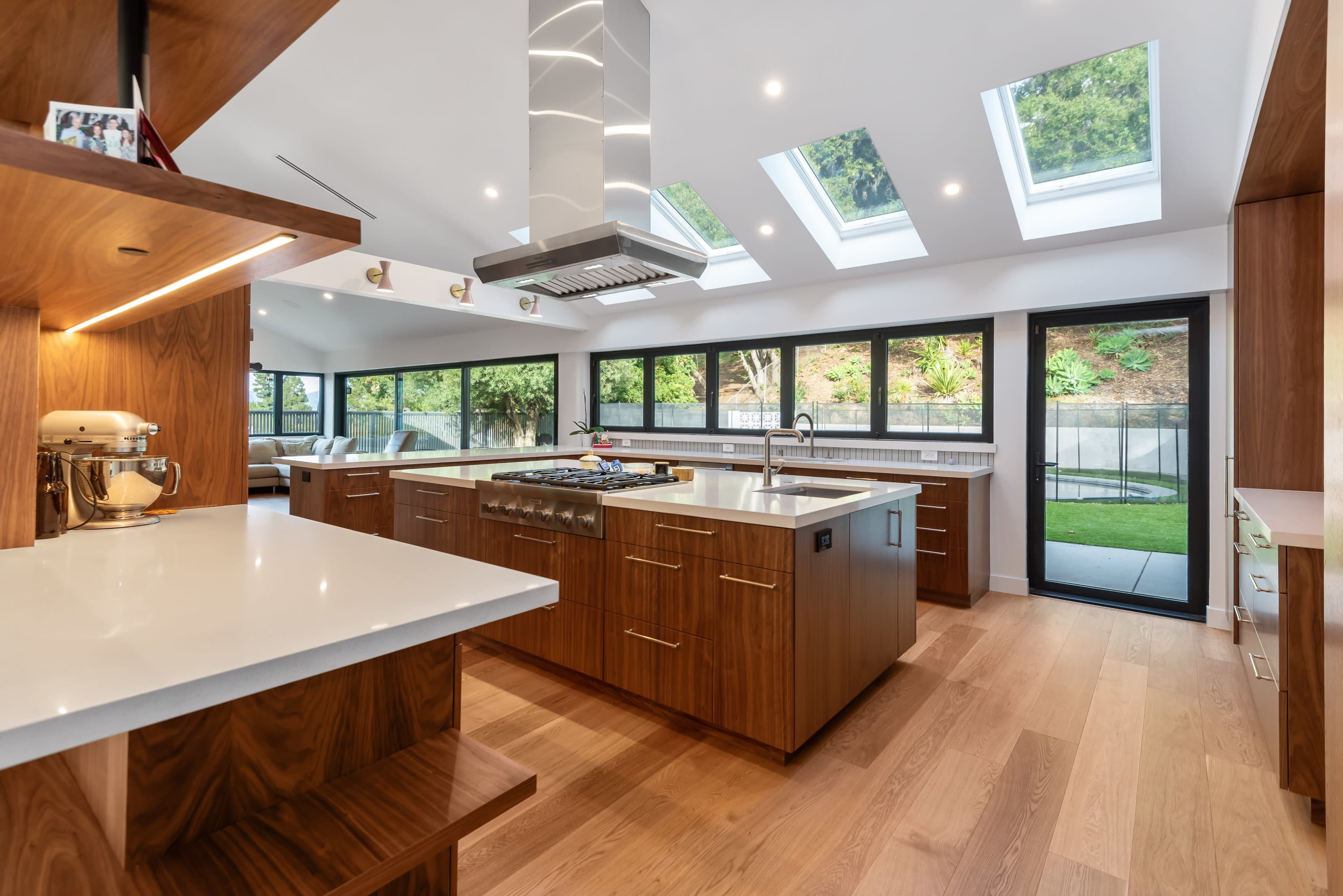 A modern kitchen featuring a large island with a gas stove, wooden cabinetry, and skylights that illuminate the space.