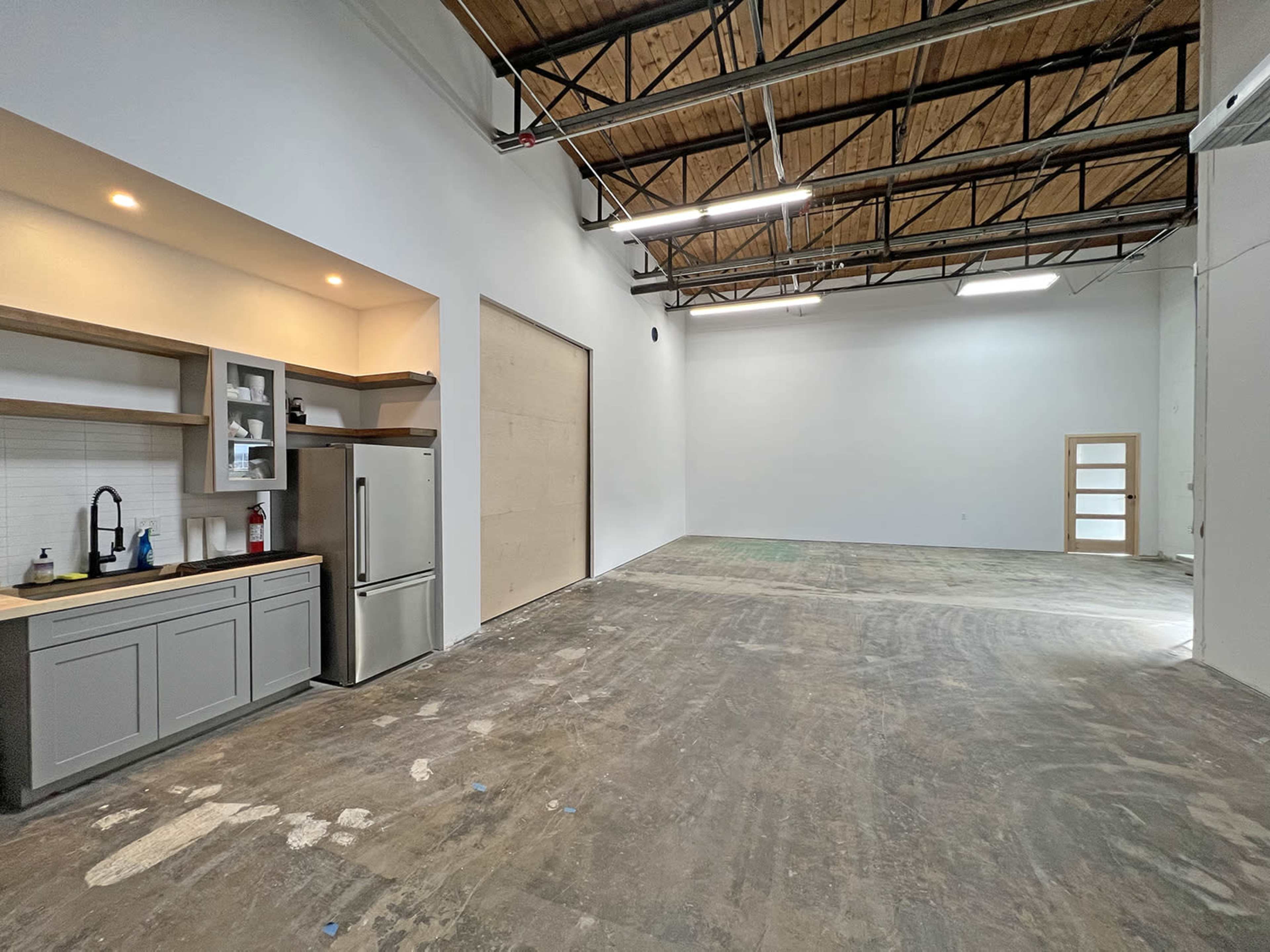 An empty industrial space with a kitchenette on one side and smooth concrete flooring.