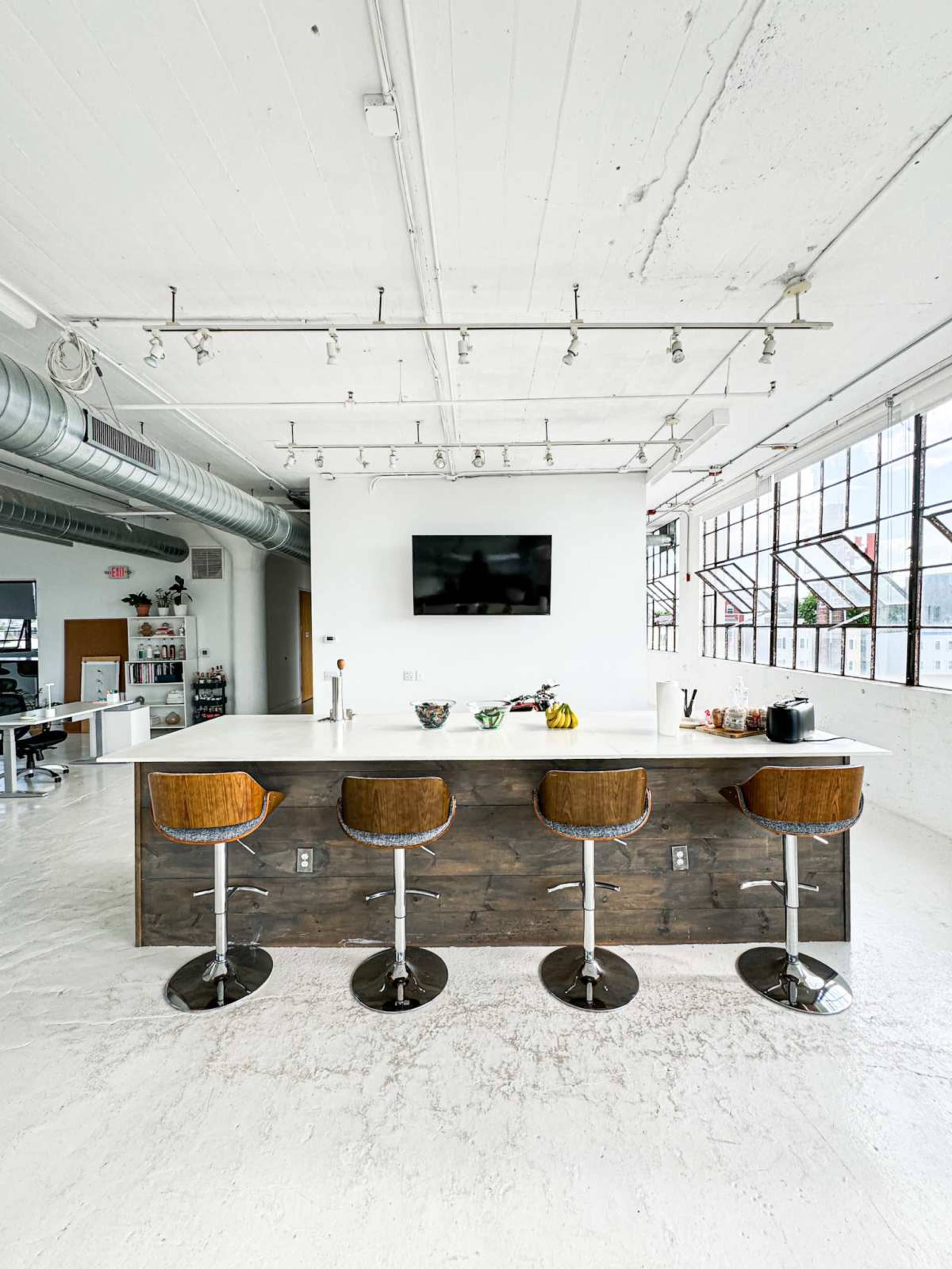 A modern kitchen features a large island with four wooden bar stools and a wall-mounted television above.