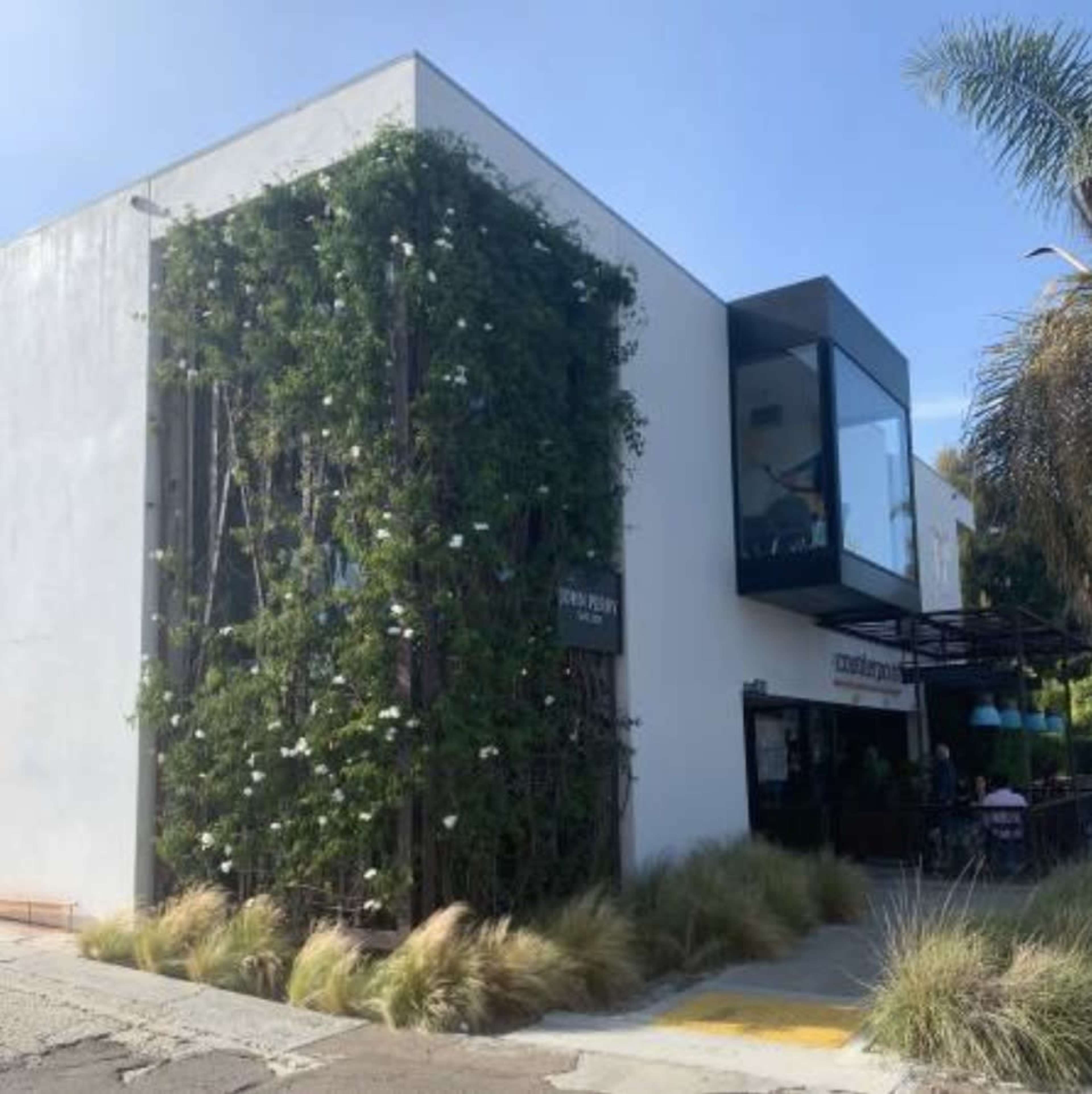 A modern building with a white exterior is partially covered in greenery, featuring a glass-enclosed upper level and landscaping in front.
