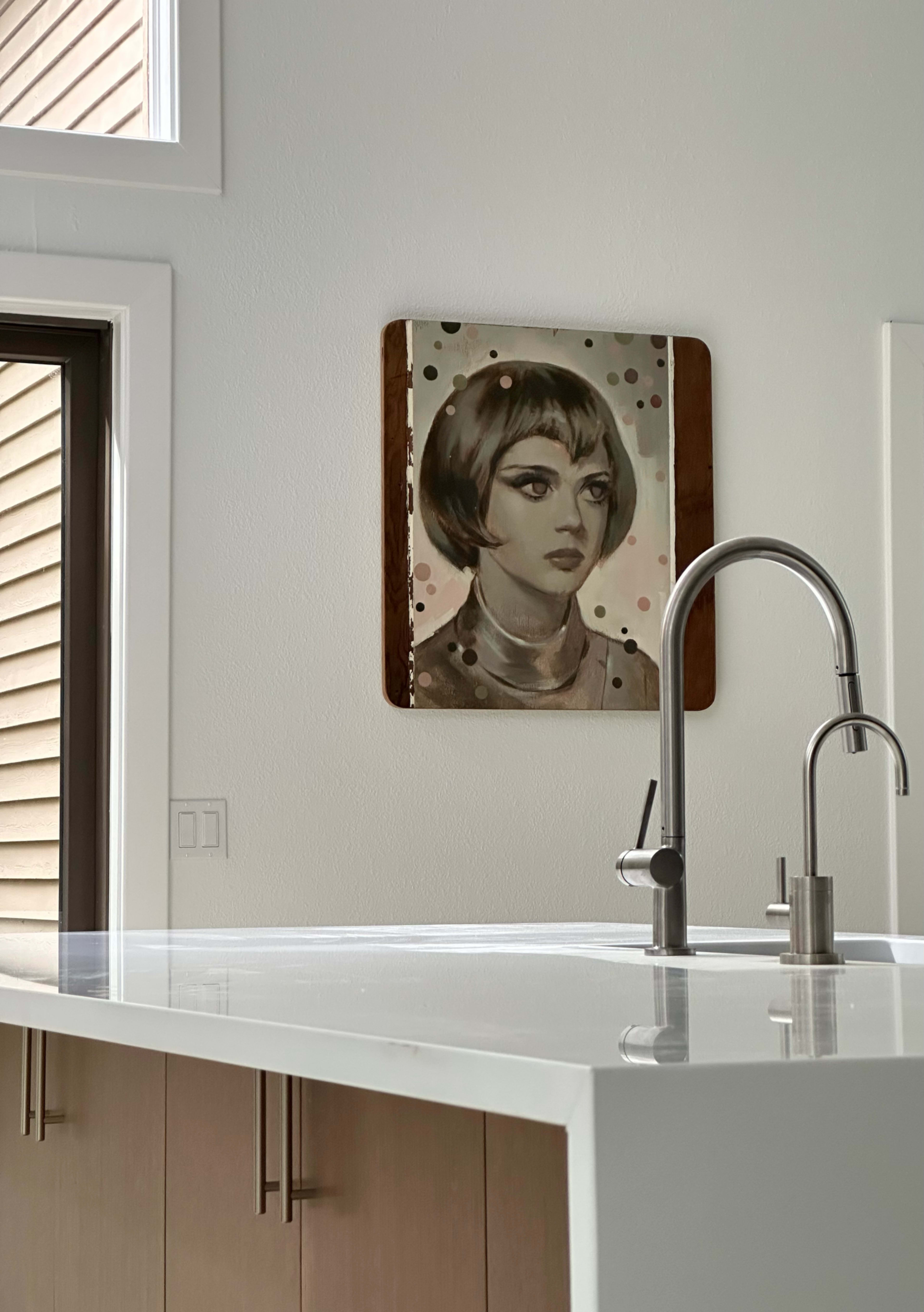 A kitchen with a modern design features a portrait of a woman hanging on the wall above a countertop with a sleek faucet.
