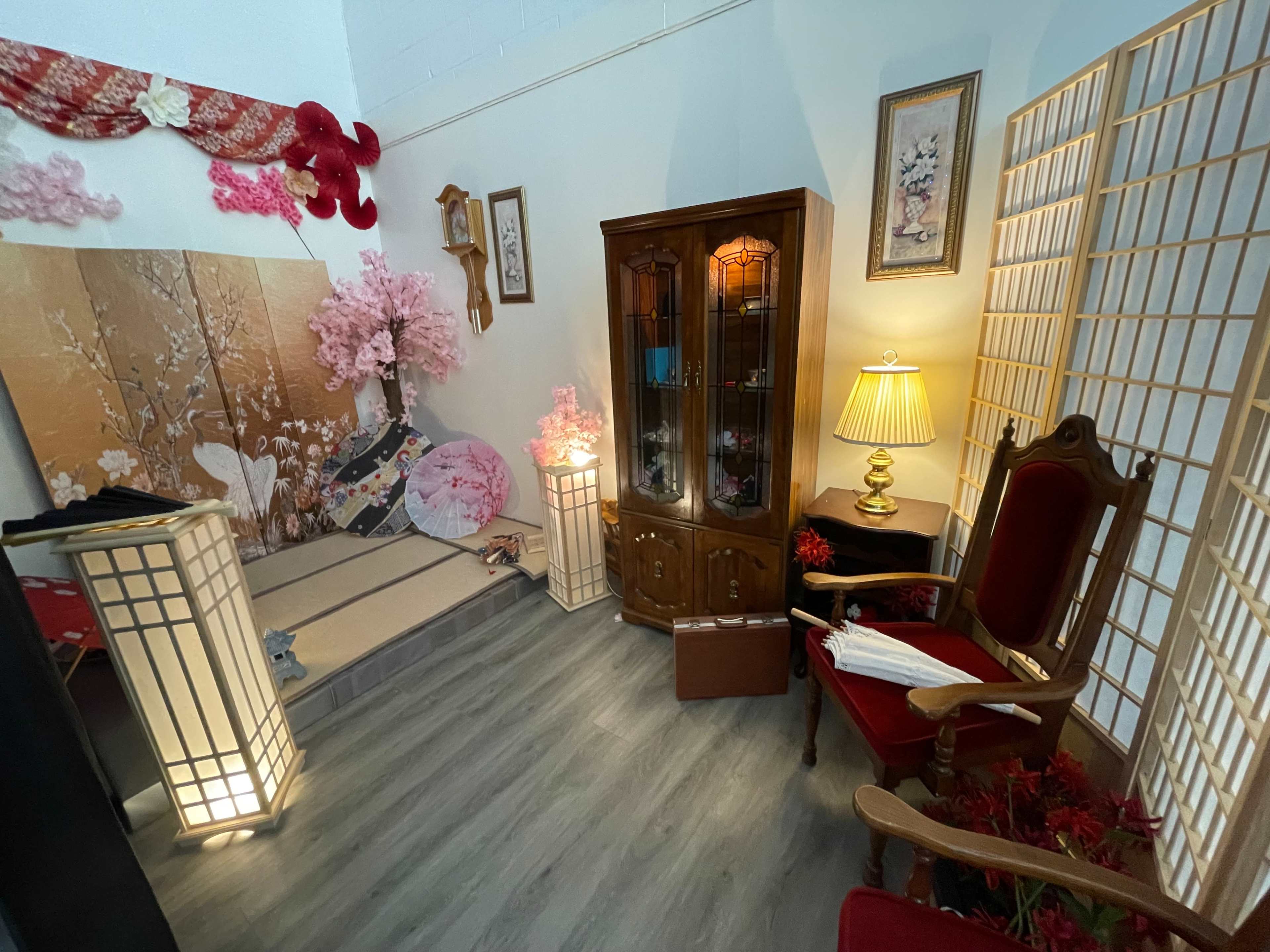 The image features a cozy room decorated with cherry blossom themes, including a wooden cabinet, an armchair, and paper lanterns.