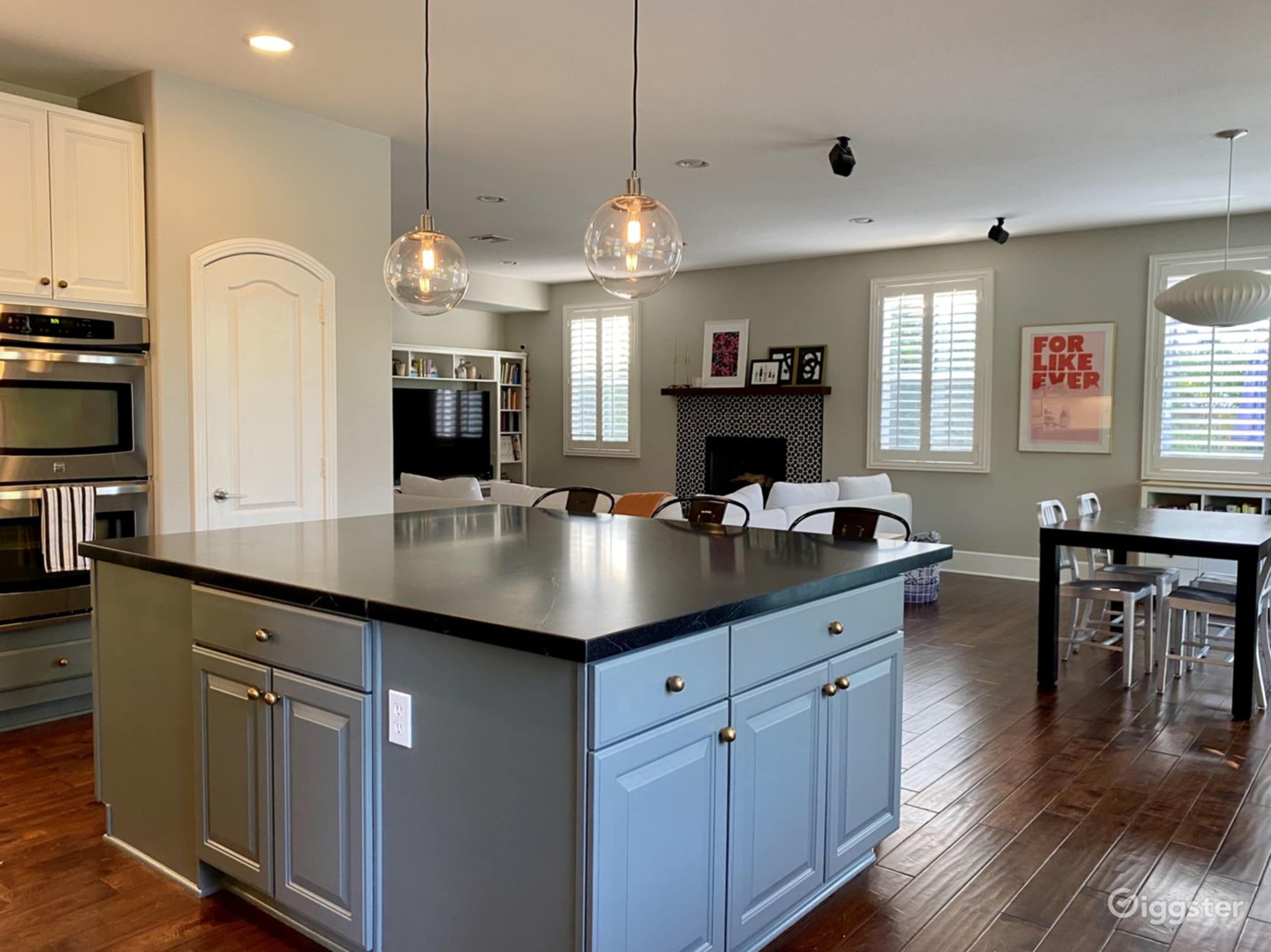A modern kitchen with an island featuring blue cabinetry, pendant lights, and a dining area in an adjacent room.