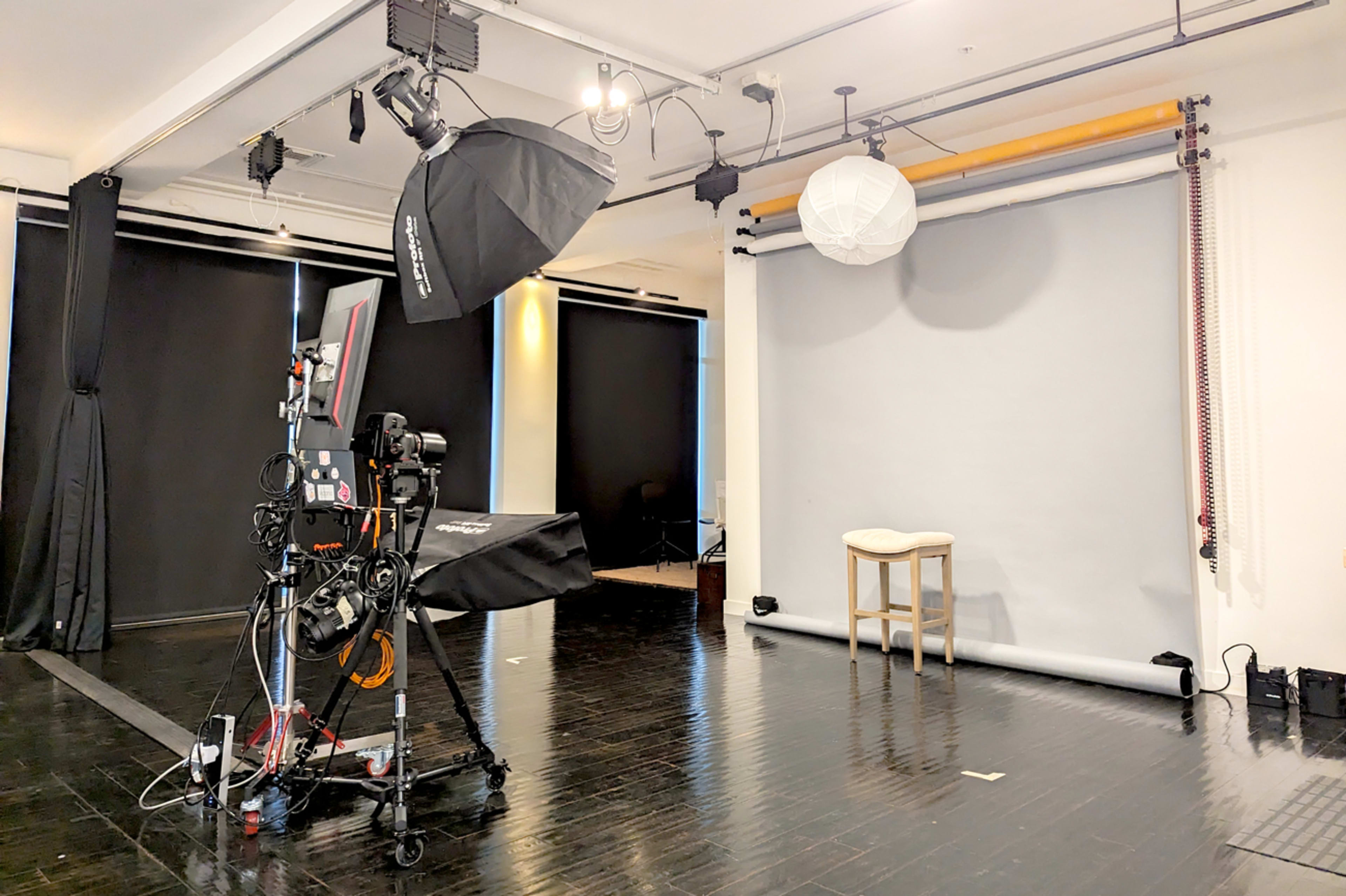 A photography studio with a camera setup, softboxes, and a neutral gray backdrop.