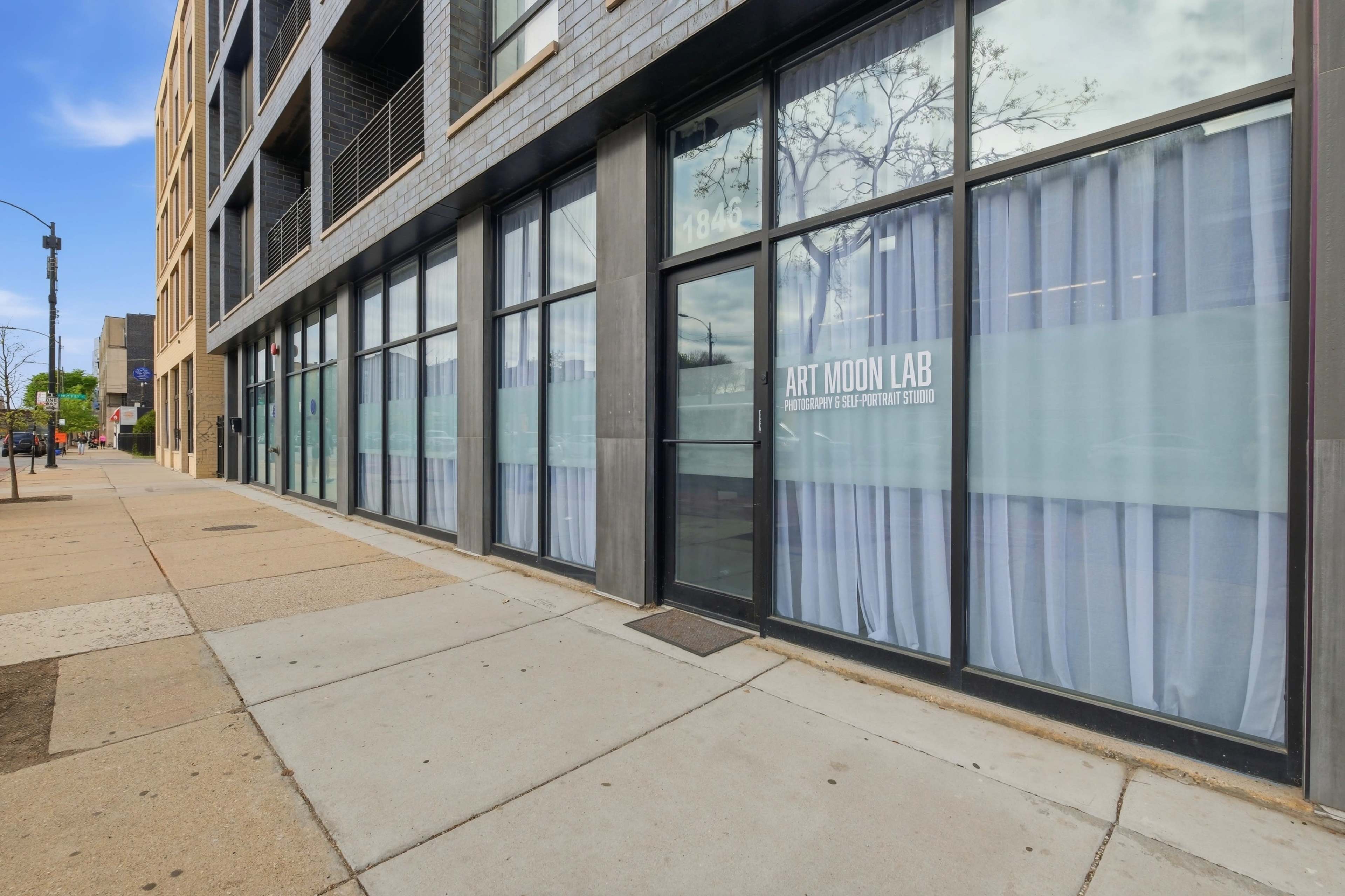 The image shows a storefront with large windows displaying white curtains and the name "Art Moon Lab" on the glass, located on a sidewalk in an urban area.