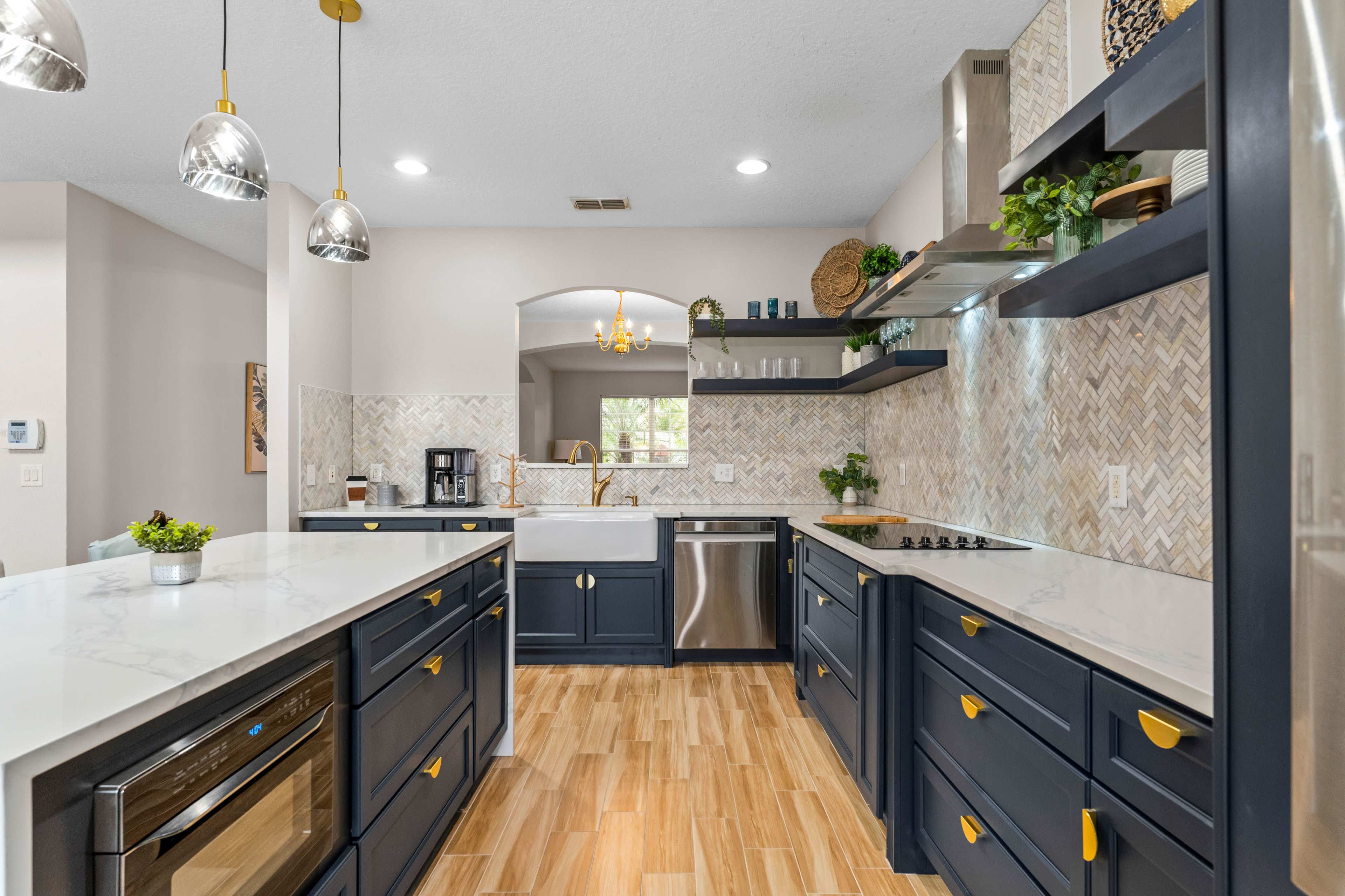 The kitchen features dark blue cabinetry, white countertops, and stainless steel appliances, with a decorative tiled backsplash and pendant lighting.