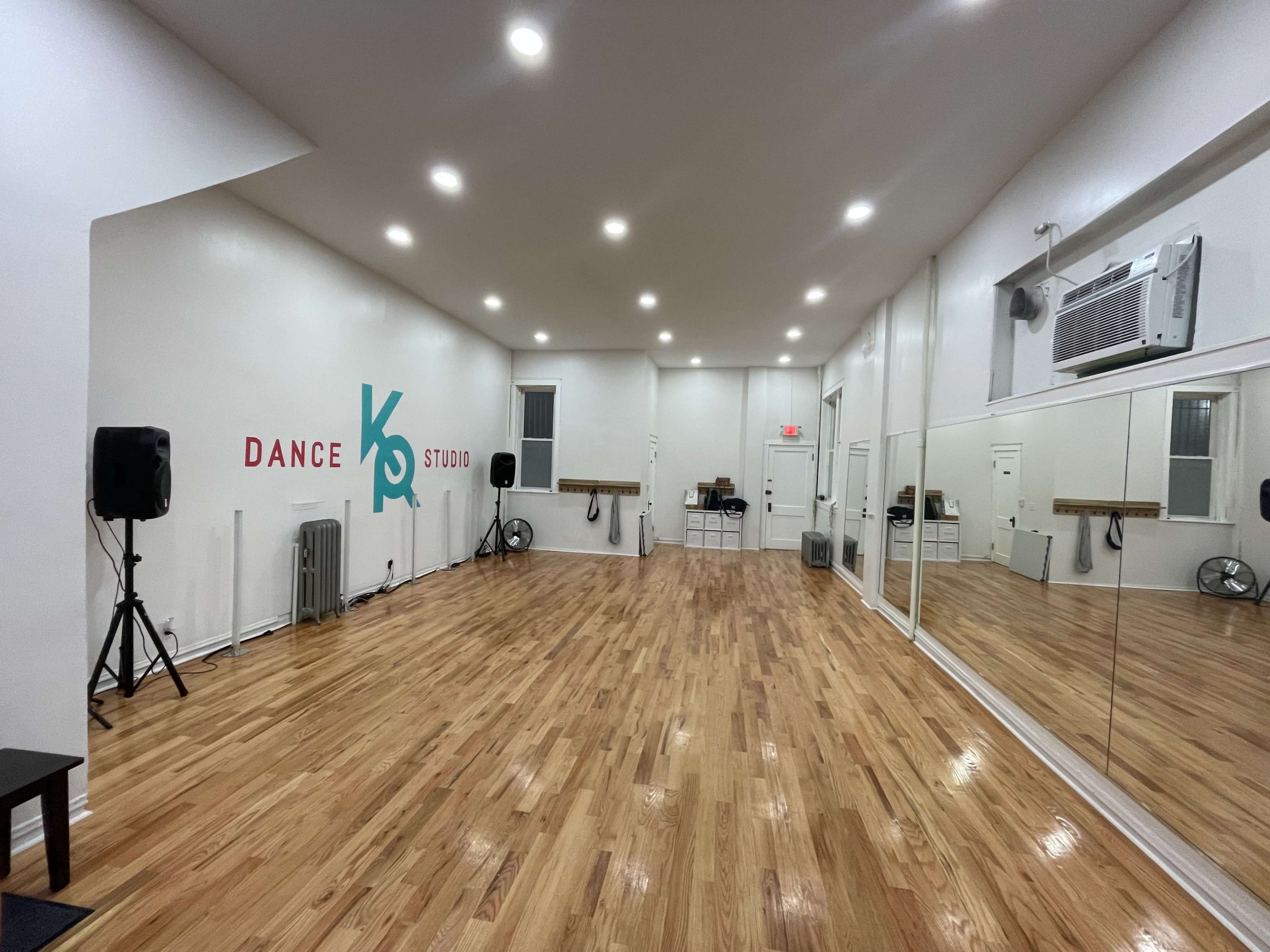 A spacious dance studio features polished wooden floors, large mirrors, and a colorful wall sign.