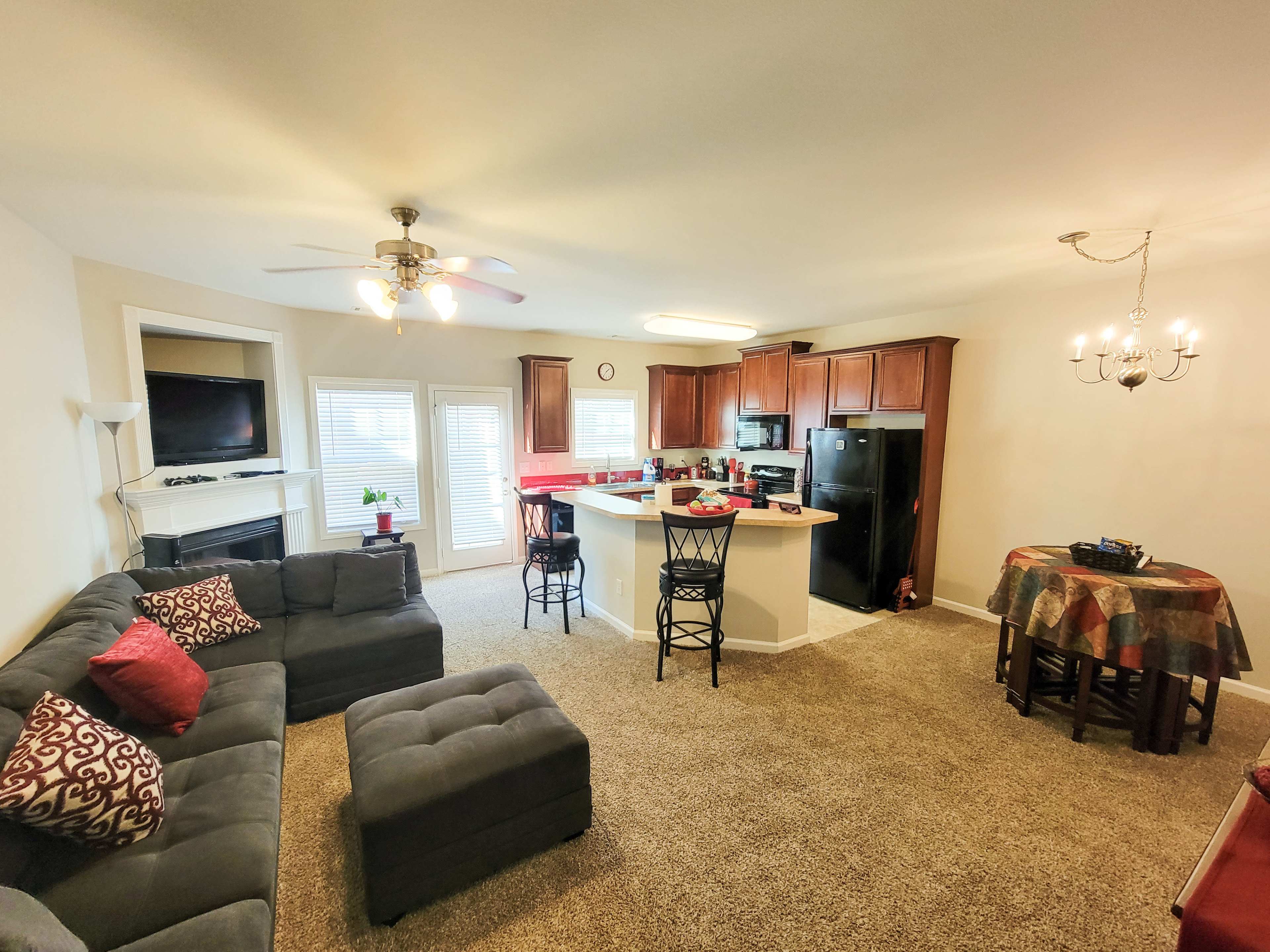 A living area with a sectional sofa, a kitchen with wooden cabinets, and a dining space featuring a round table and chairs.