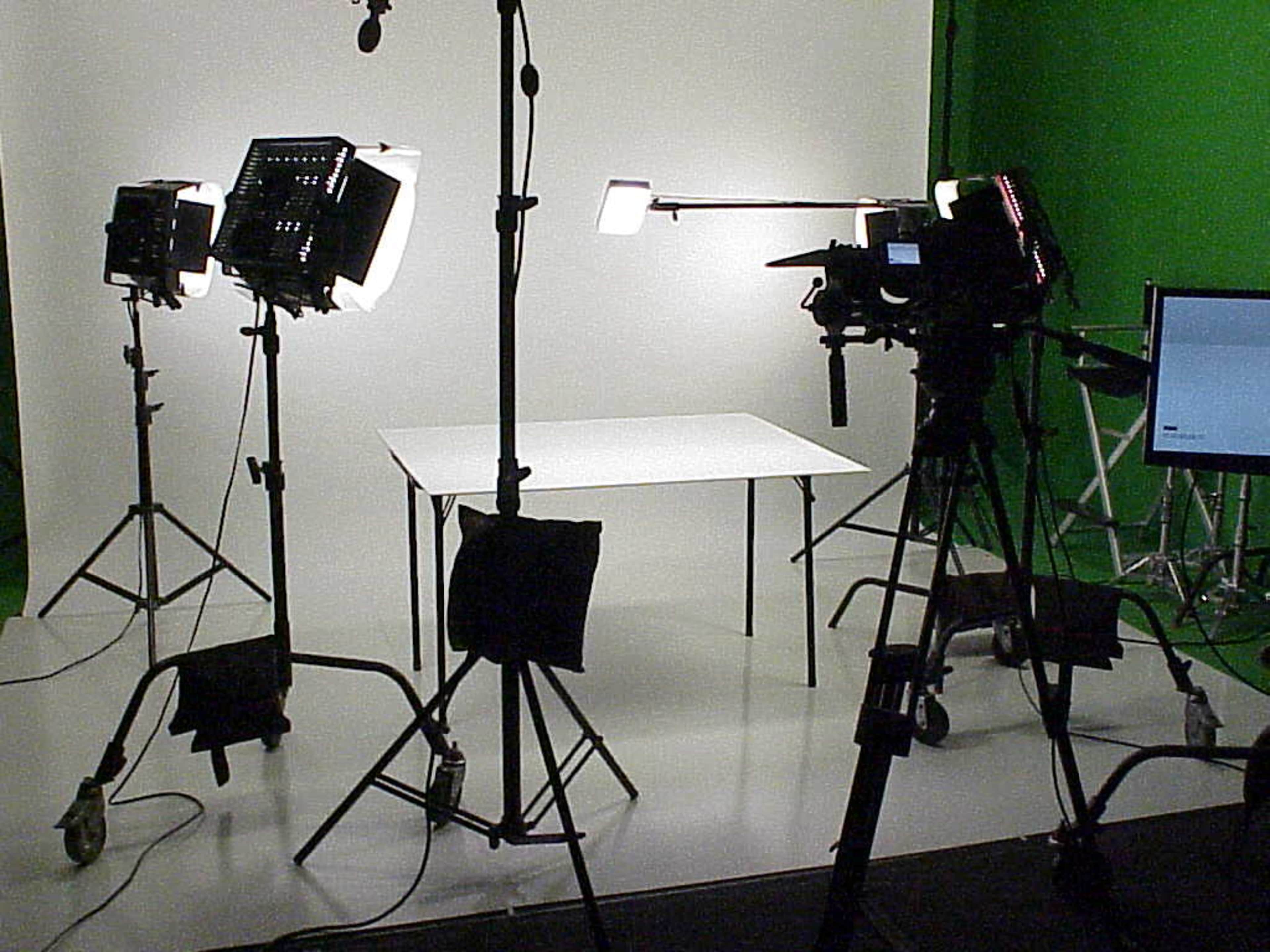 A photography studio is set up with cameras and lights positioned around a white table against a green backdrop.