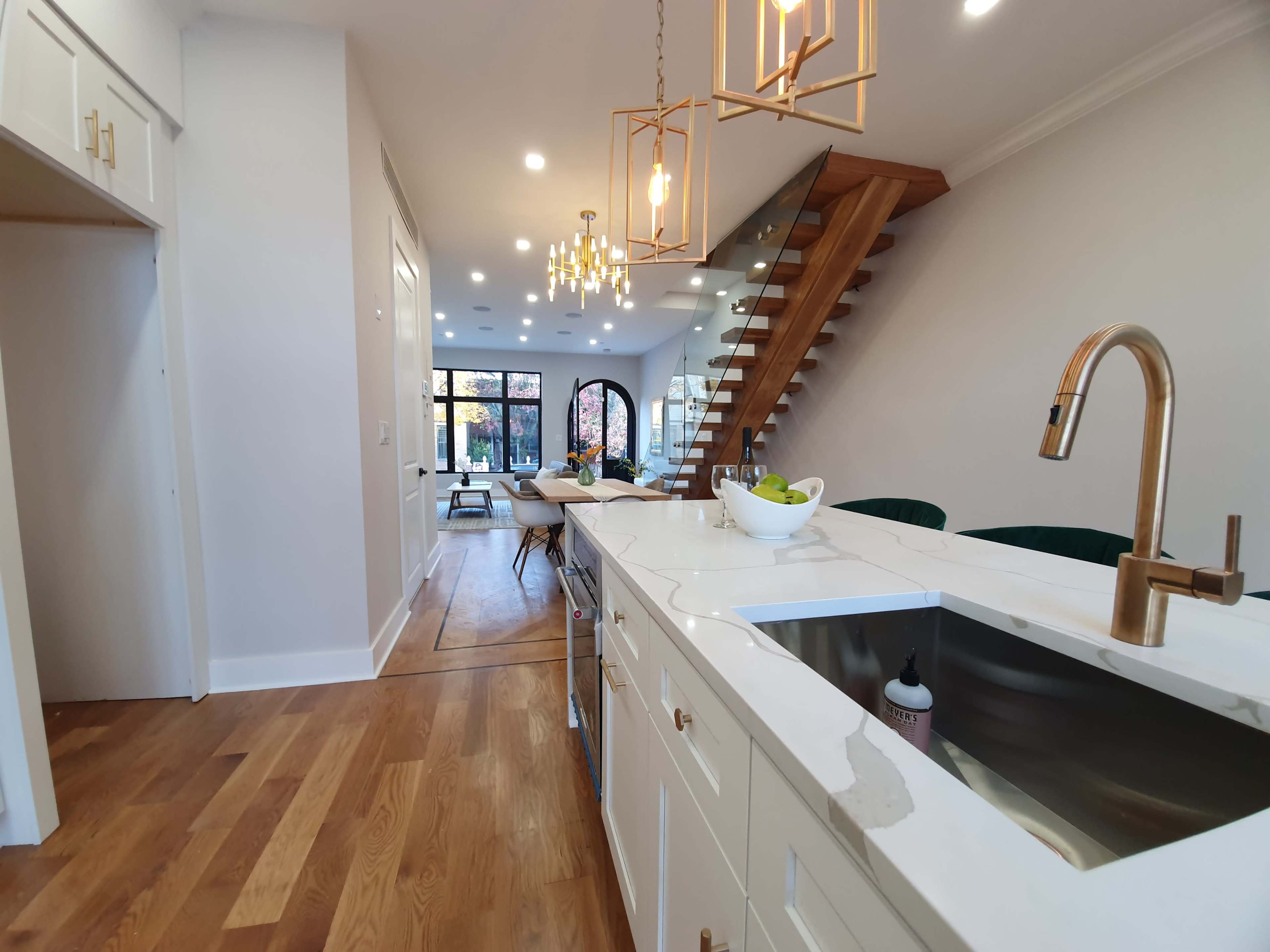 A modern kitchen with a marble countertop, gold fixtures, and a view of a staircase leading to an open living area with large windows.