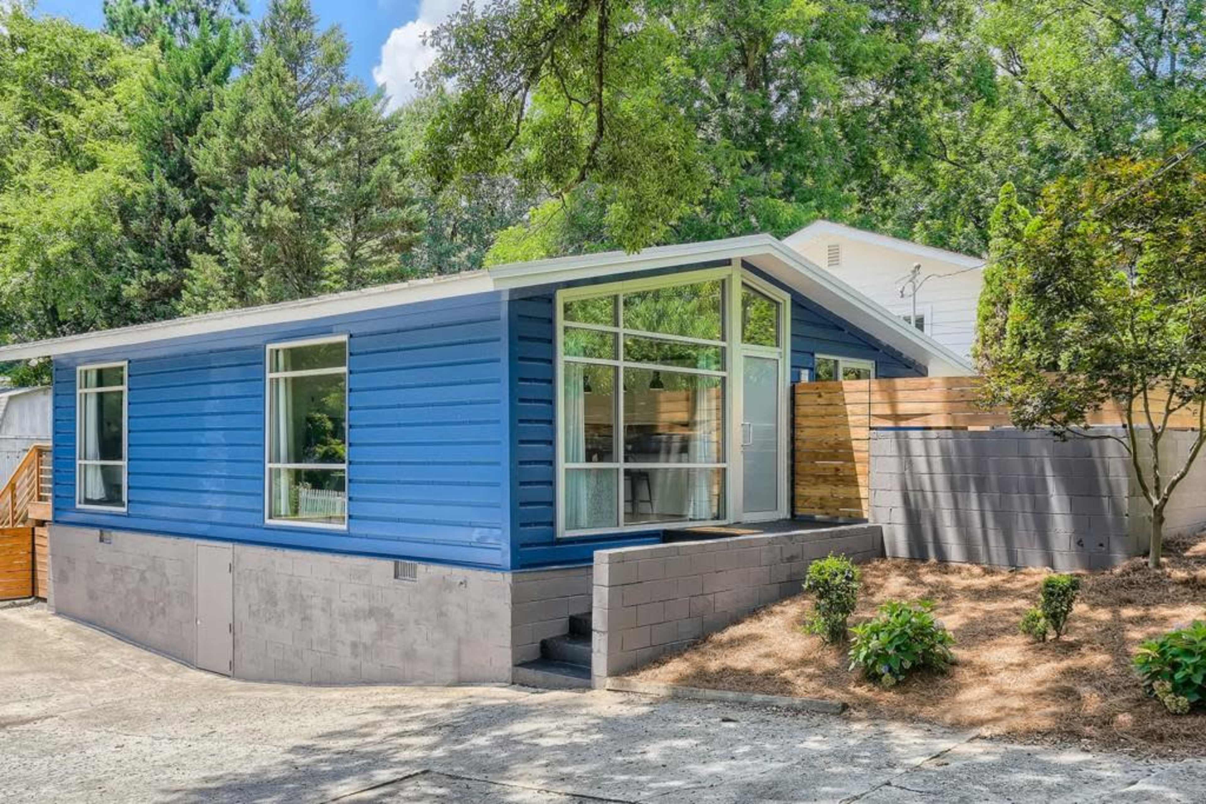 A modern blue house with large windows, a landscaped front yard, and a gravel driveway.