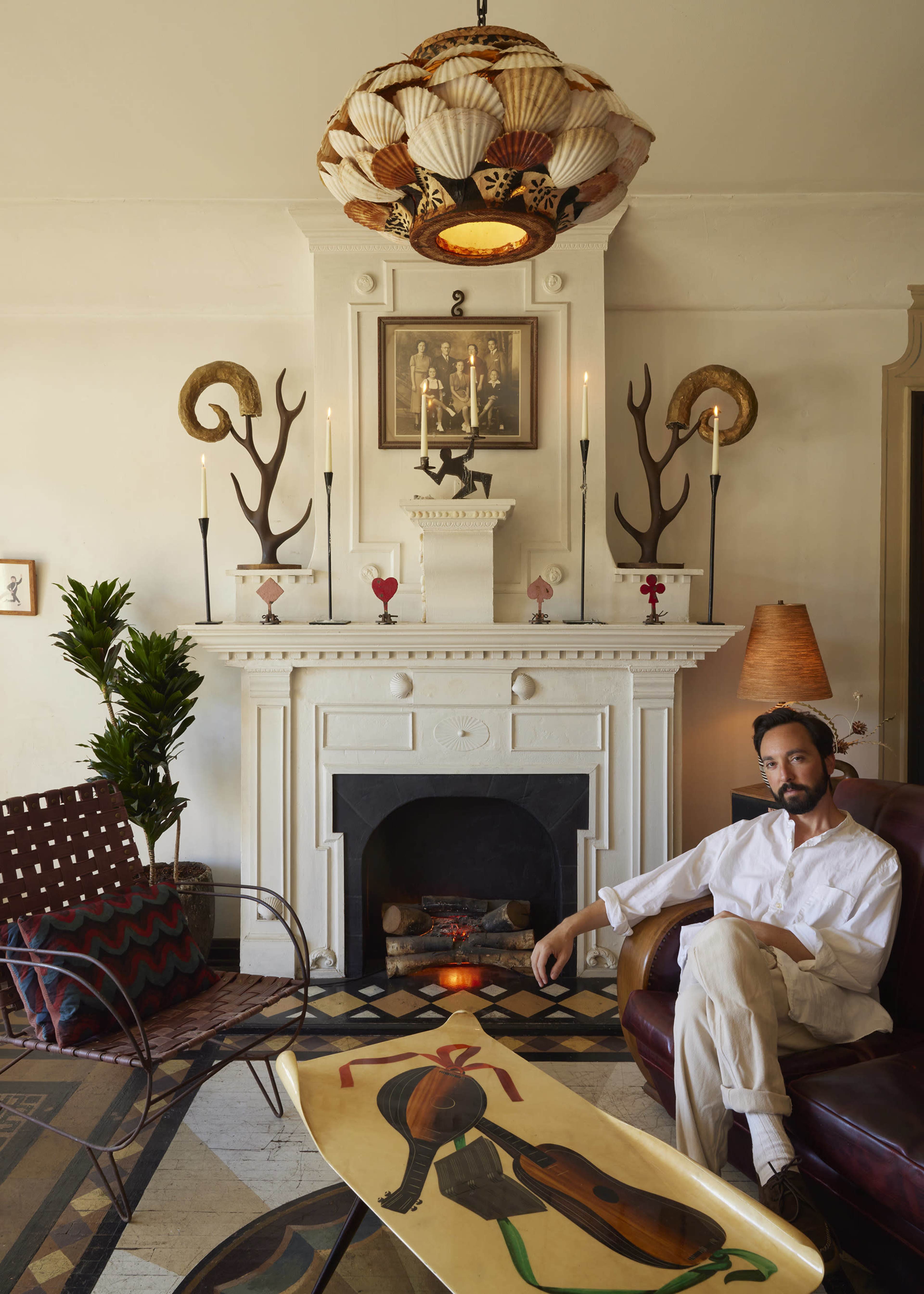 A man sits in a leather chair in a stylish living room featuring a decorative fireplace and an artistic coffee table.
