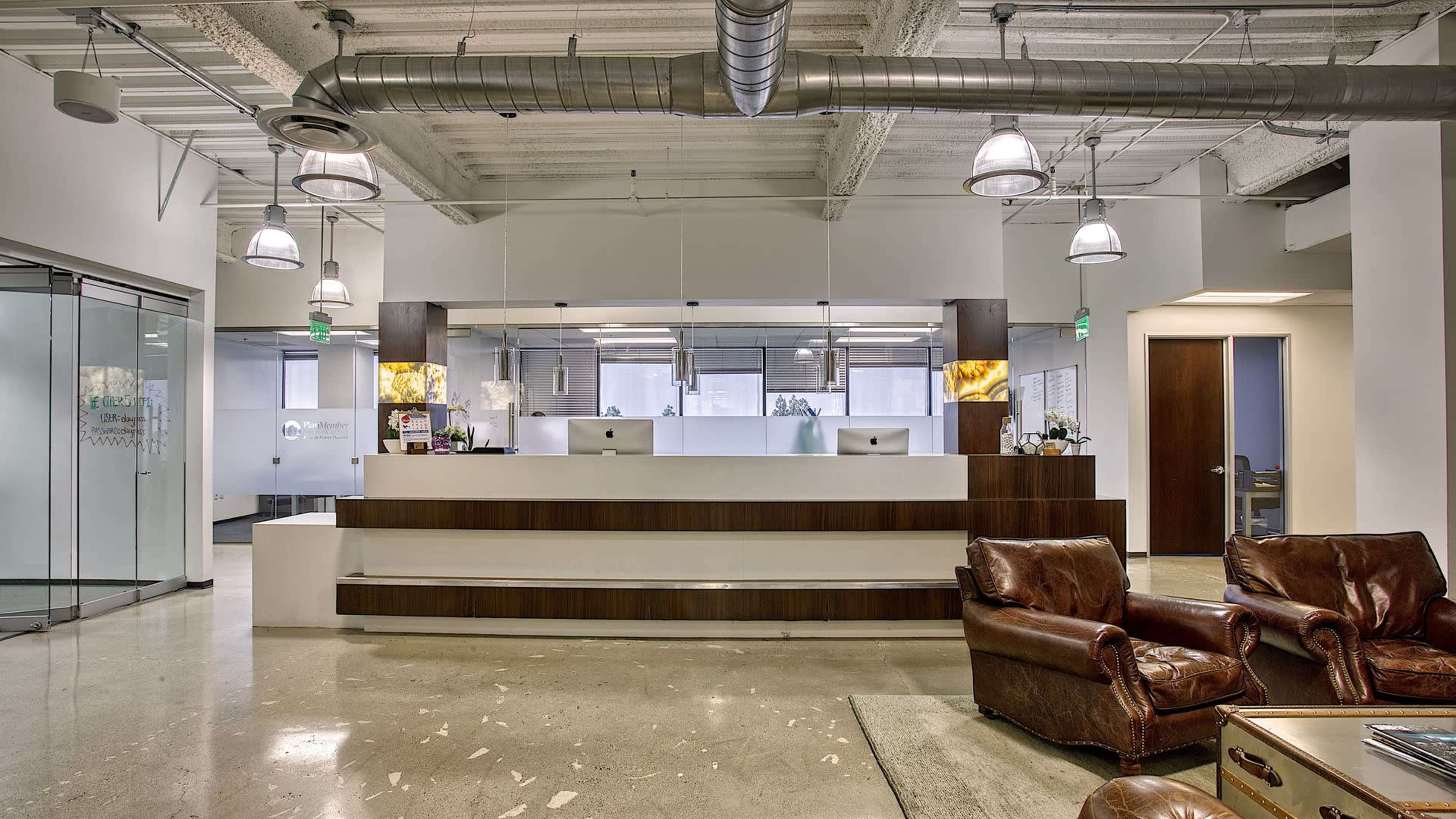 The image shows a modern office reception area with a sleek front desk, two computers, and brown leather chairs.