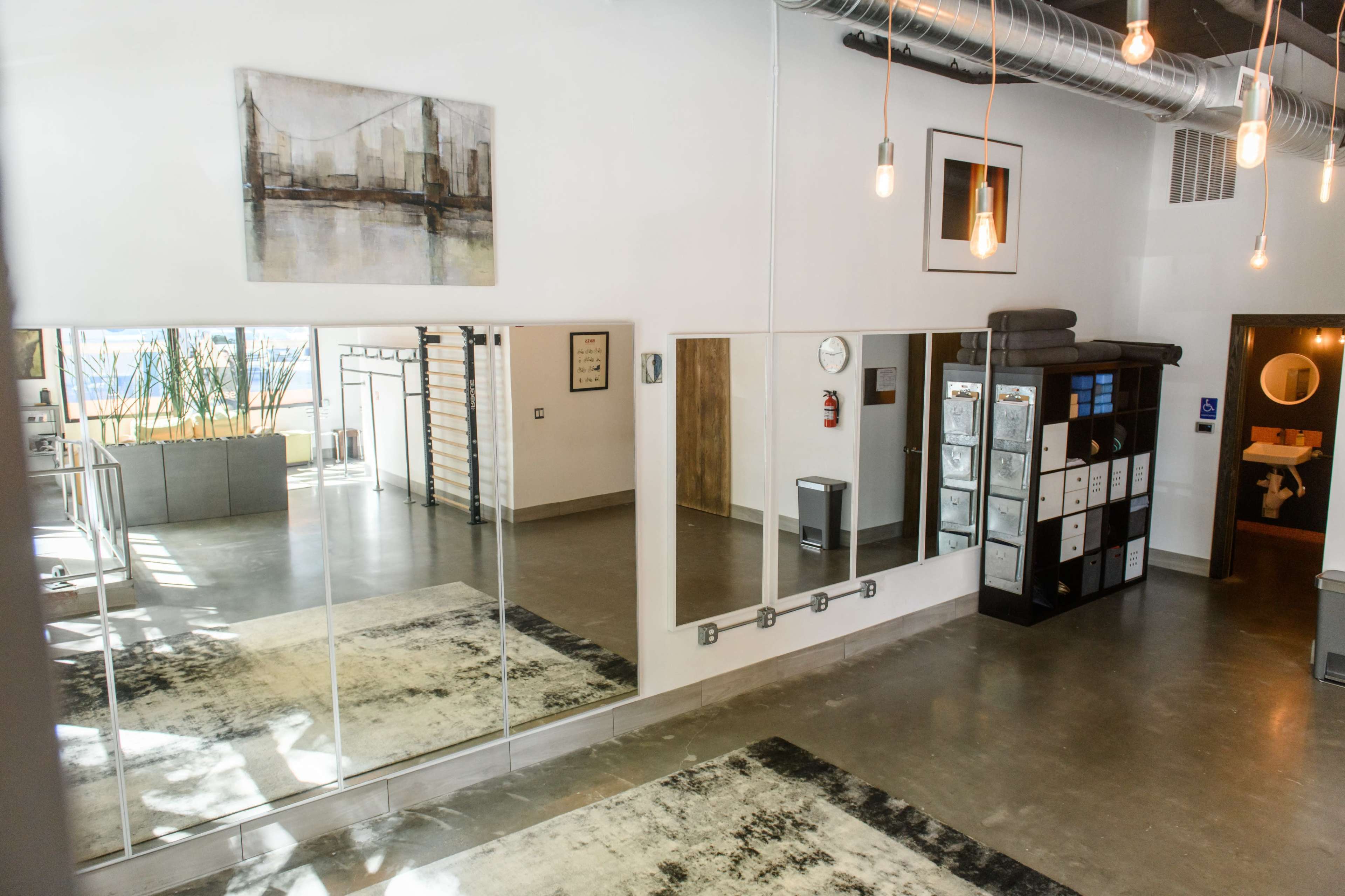 The interior of a modern, well-lit space features large mirrors, a rug, and storage units, with artwork displayed on the walls.