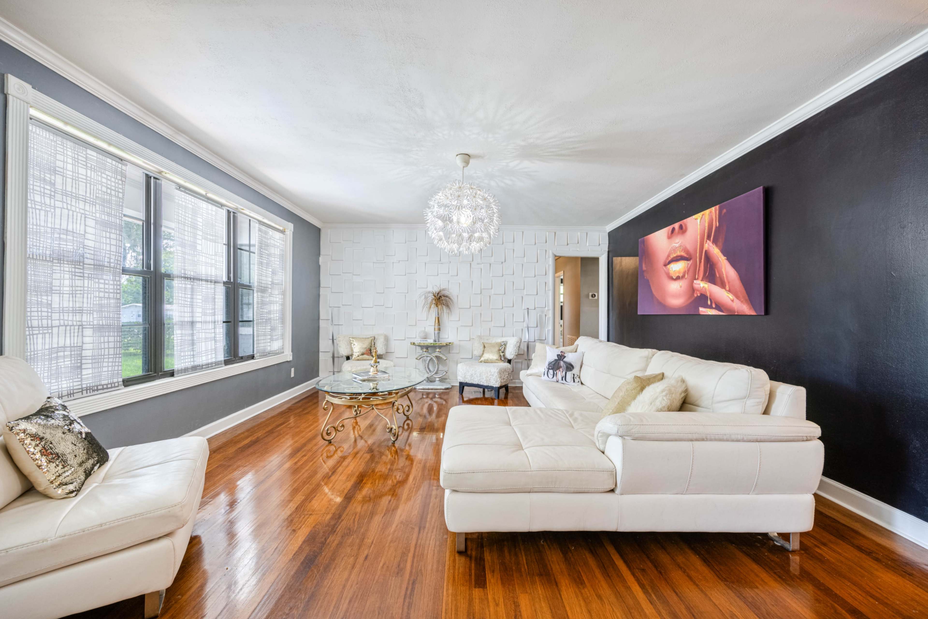 The living room features a white sectional sofa, a glass coffee table, and a modern chandelier, with large windows providing natural light.