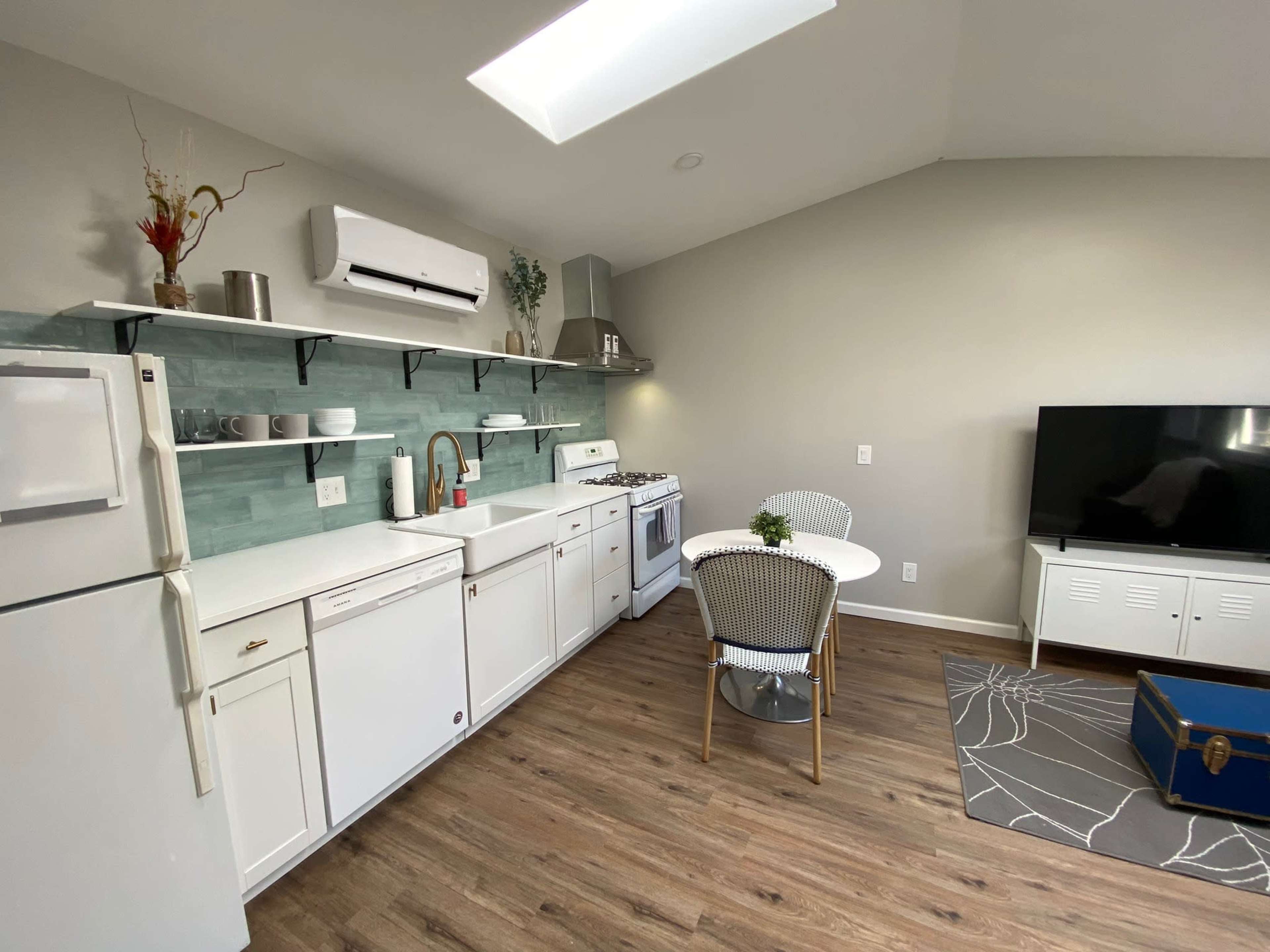 The image shows a modern kitchen with white cabinetry, a gas stove, and a small dining area featuring a round table and chairs.
