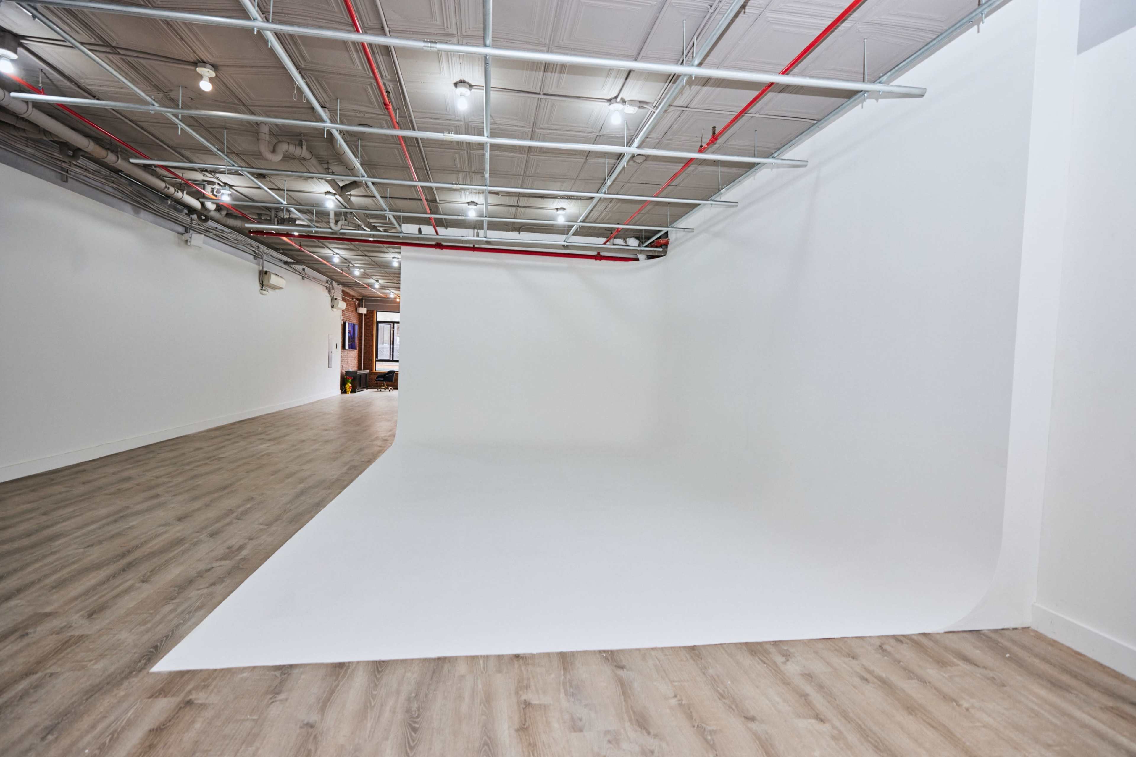 A spacious studio with a seamless white backdrop, wooden flooring, and exposed ceiling fixtures.