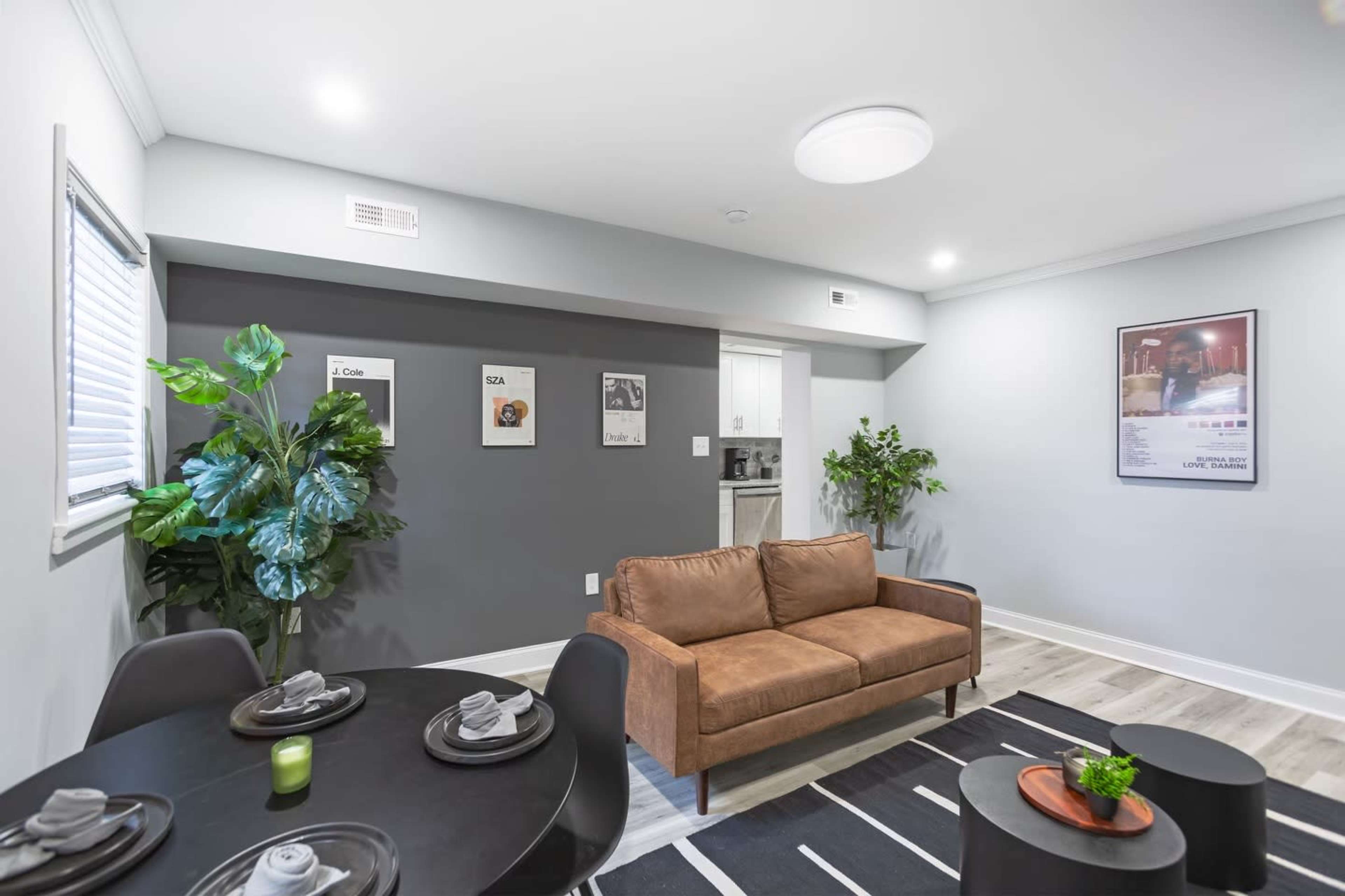 A modern living space with a brown couch, a round dining table set for four, and potted plants against a gray wall.