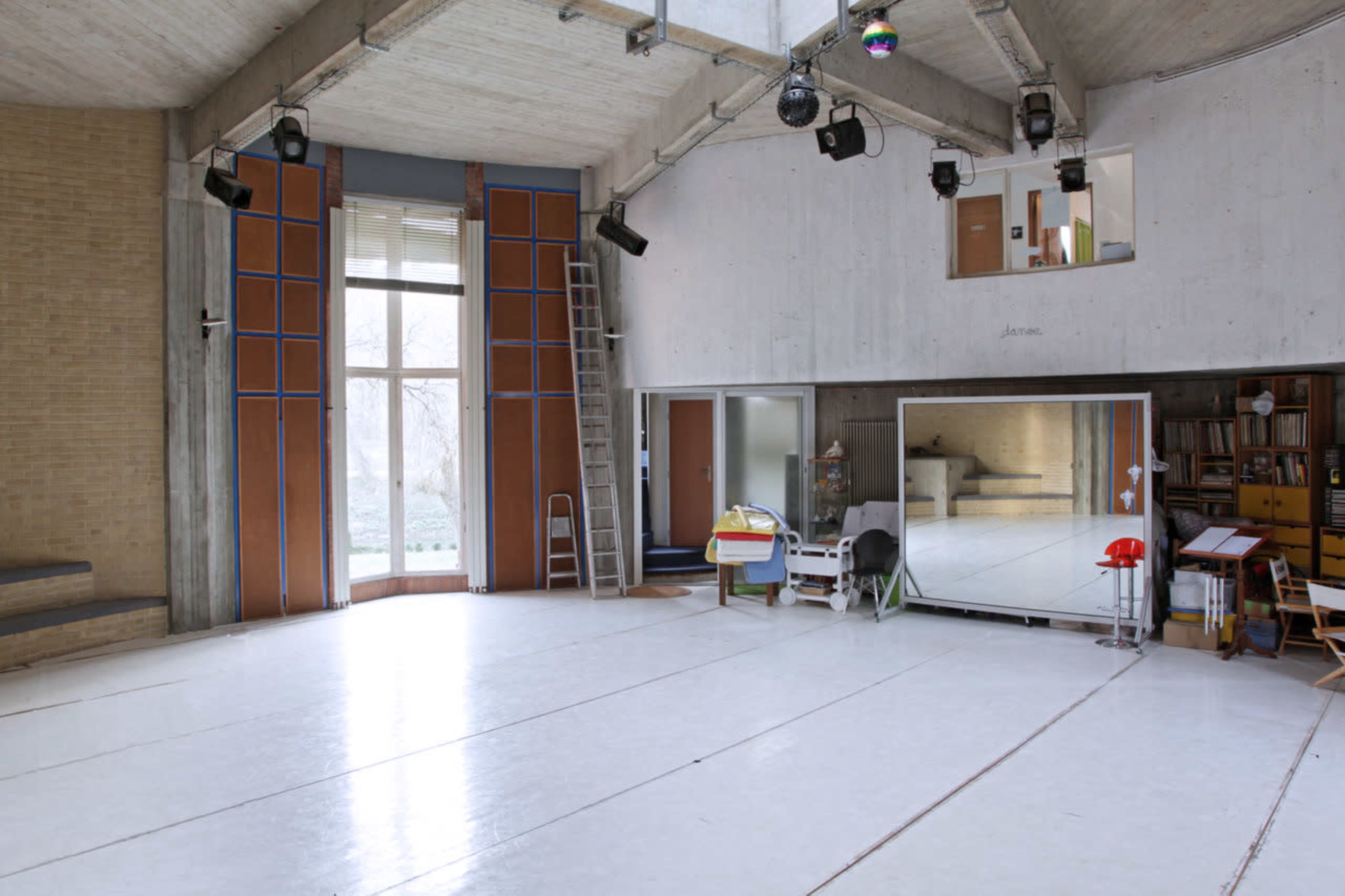 A spacious, minimalist studio with large mirrors, wooden accents, and ample natural light coming through a large window.