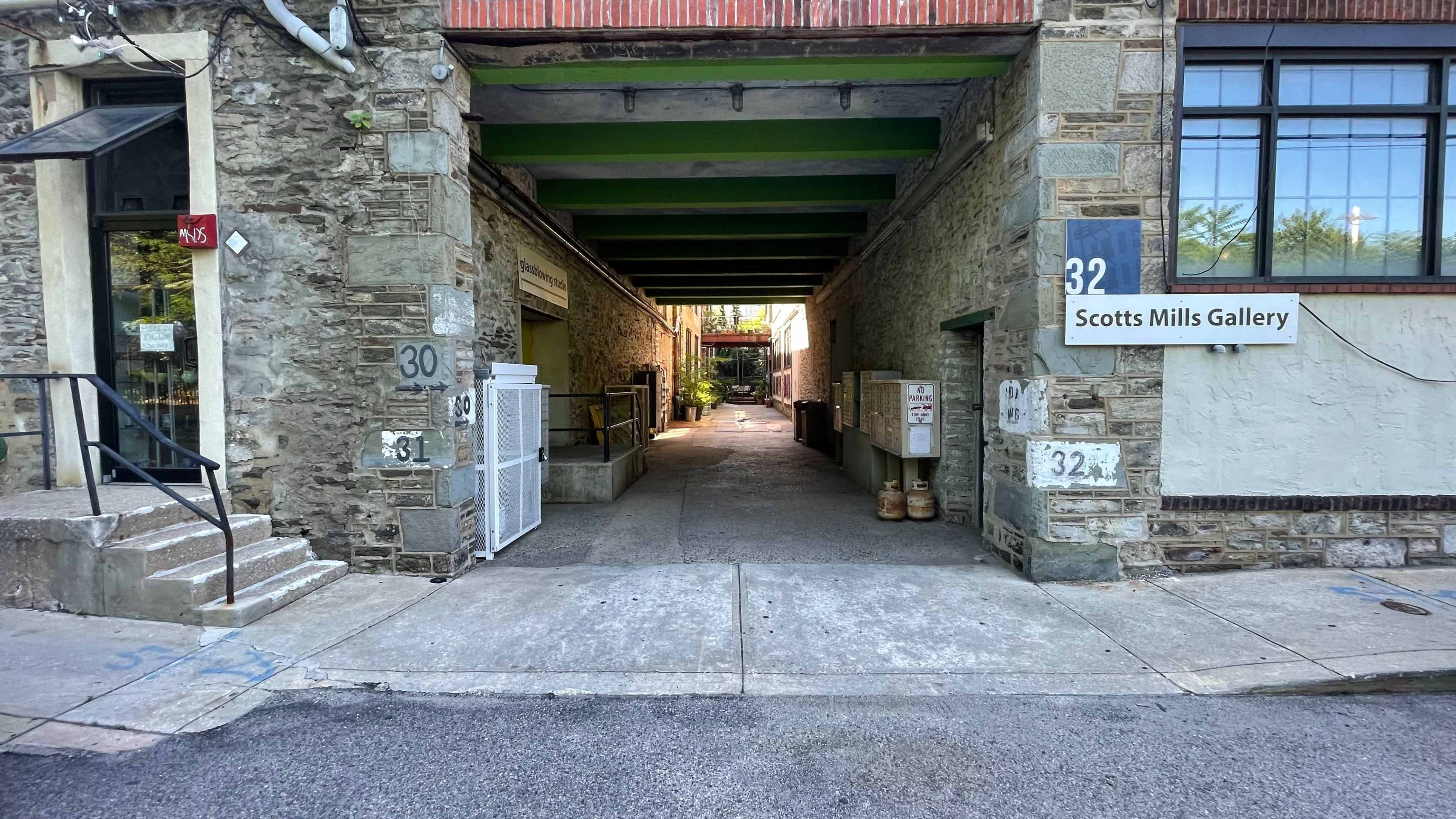 The image shows a narrow passageway between stone buildings leading to a courtyard, with signage for "Scotts Mills Gallery" on the right.
