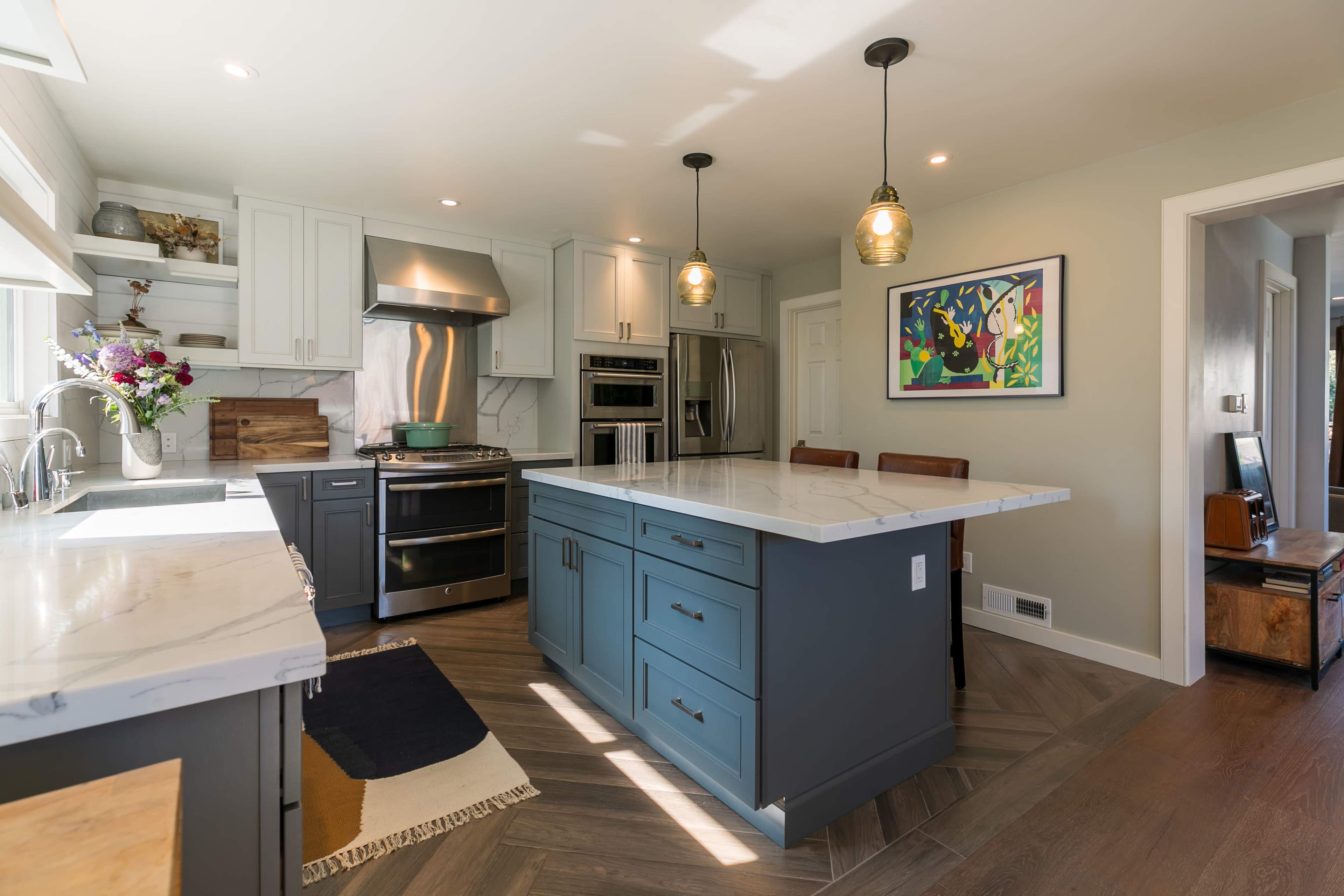 A modern kitchen featuring light cabinetry, a large island with a marble countertop, and stainless steel appliances.