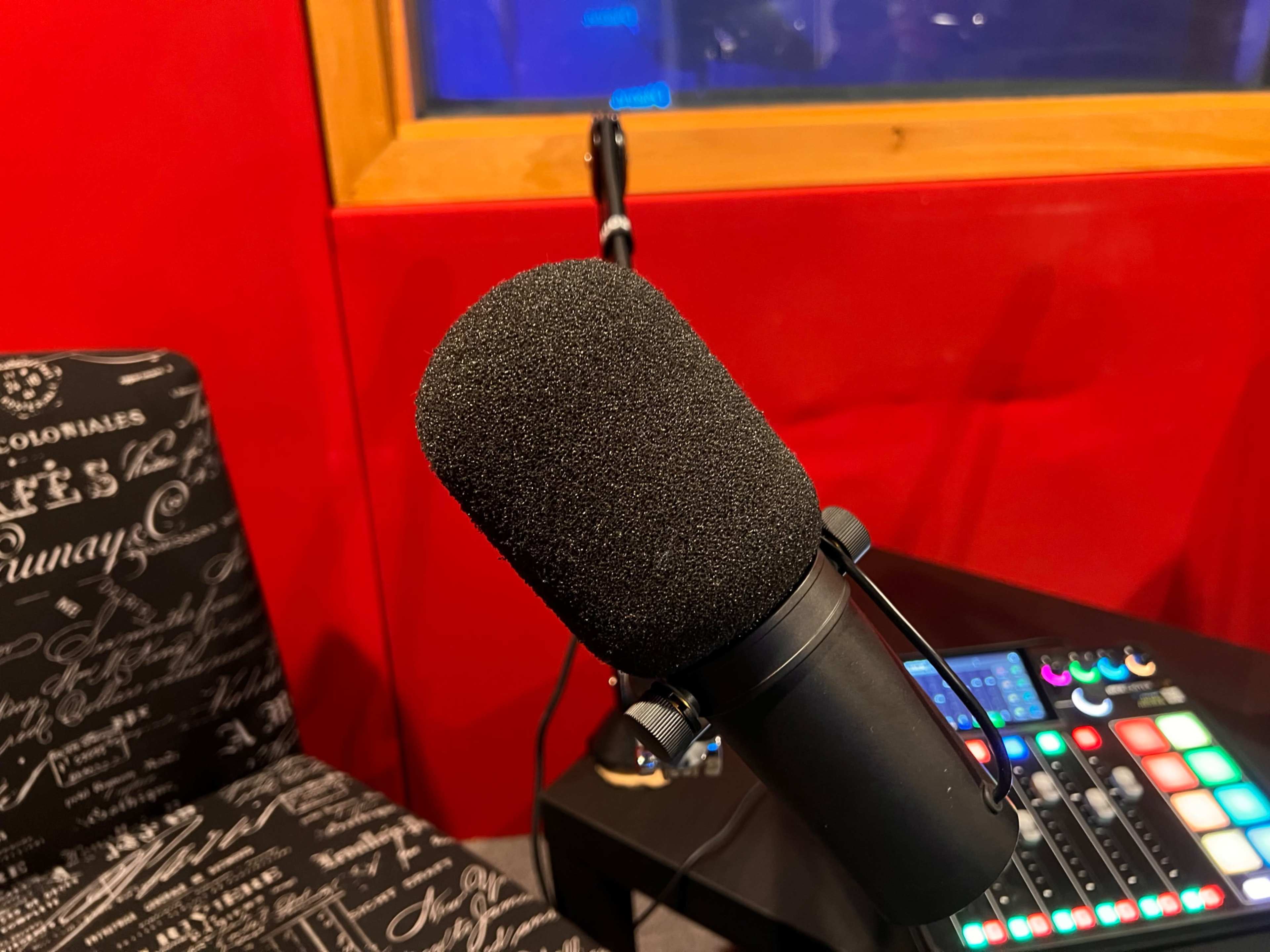 A black microphone stands in front of a red wall, with a sound mixer on a nearby table.