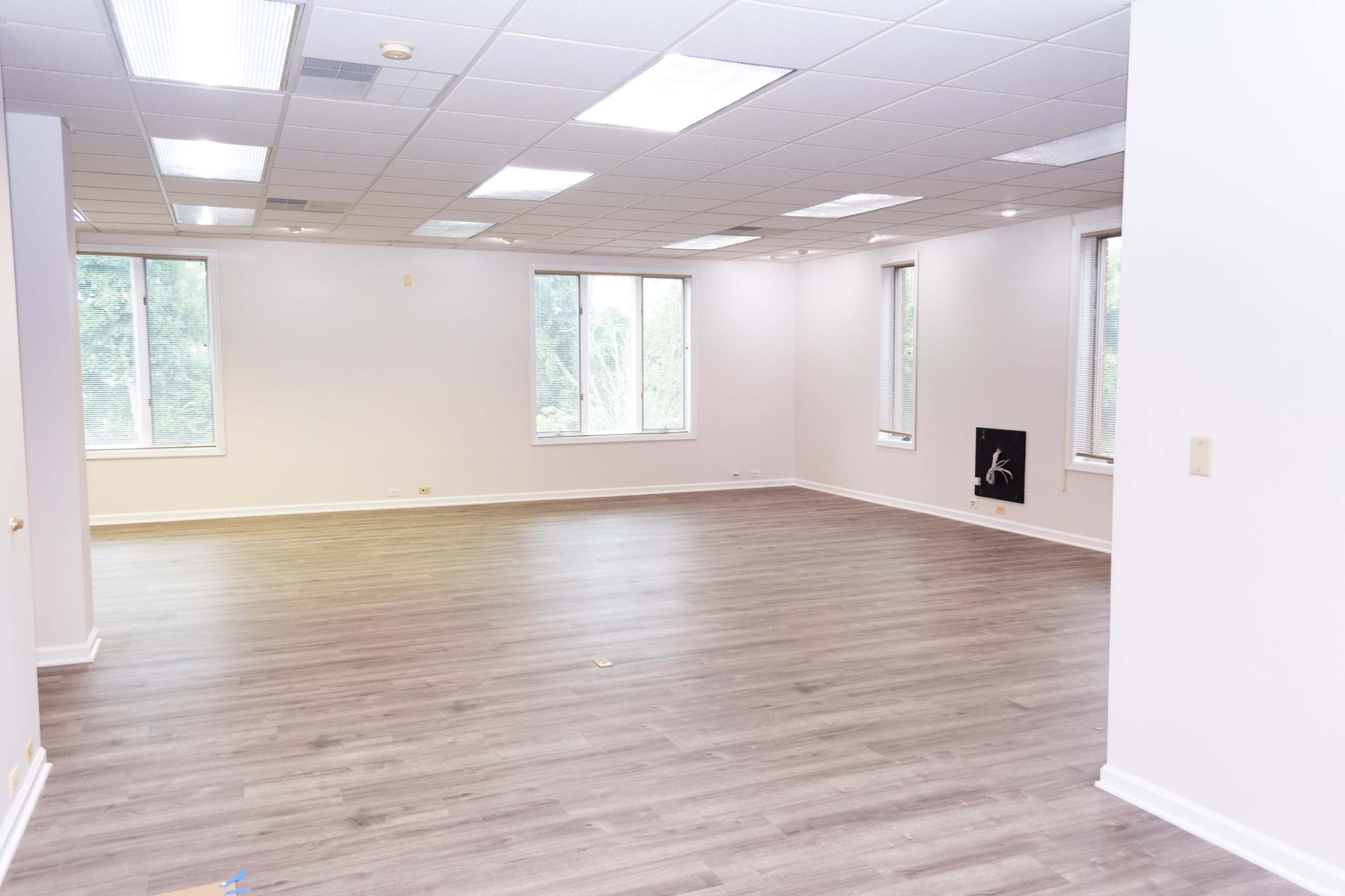 An empty, unfurnished room with large windows and wood laminate flooring.