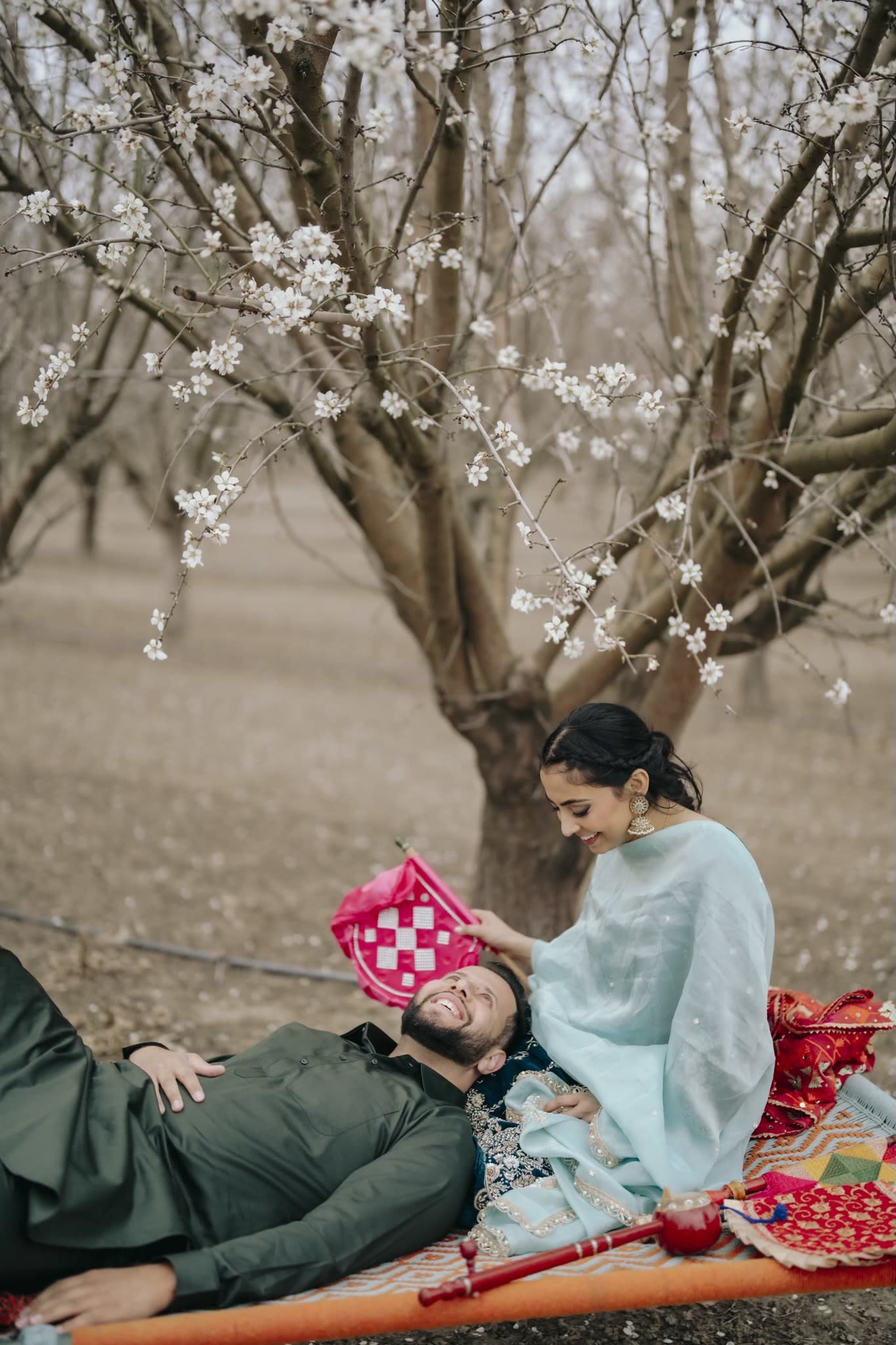 A couple relaxes together on a colorful blanket under blossoming trees in a serene outdoor setting.