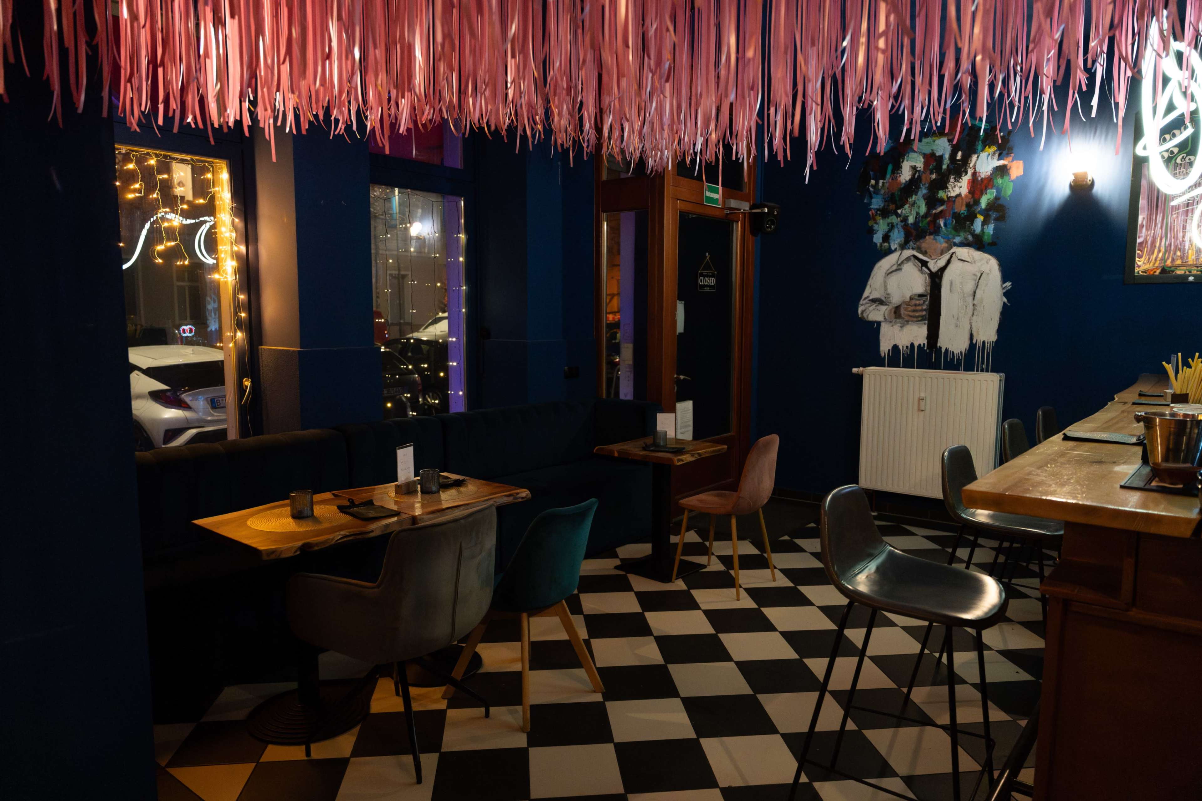 The image shows an indoor area of a restaurant featuring colorful seating, a checkered floor, and decorative elements, including pink streamers and illuminated displays.