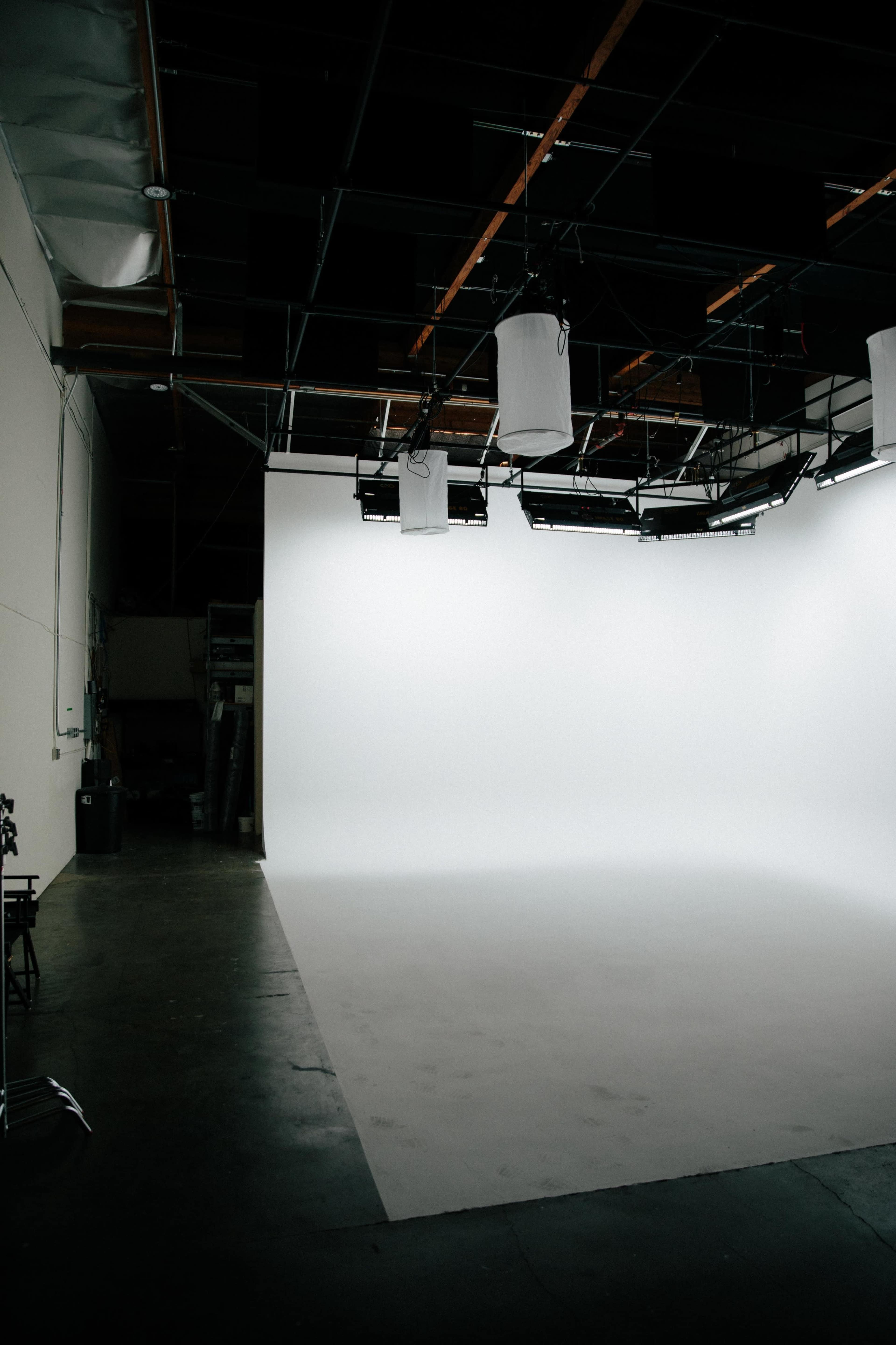 The image shows a spacious studio with a white backdrop and overhead lighting equipment.