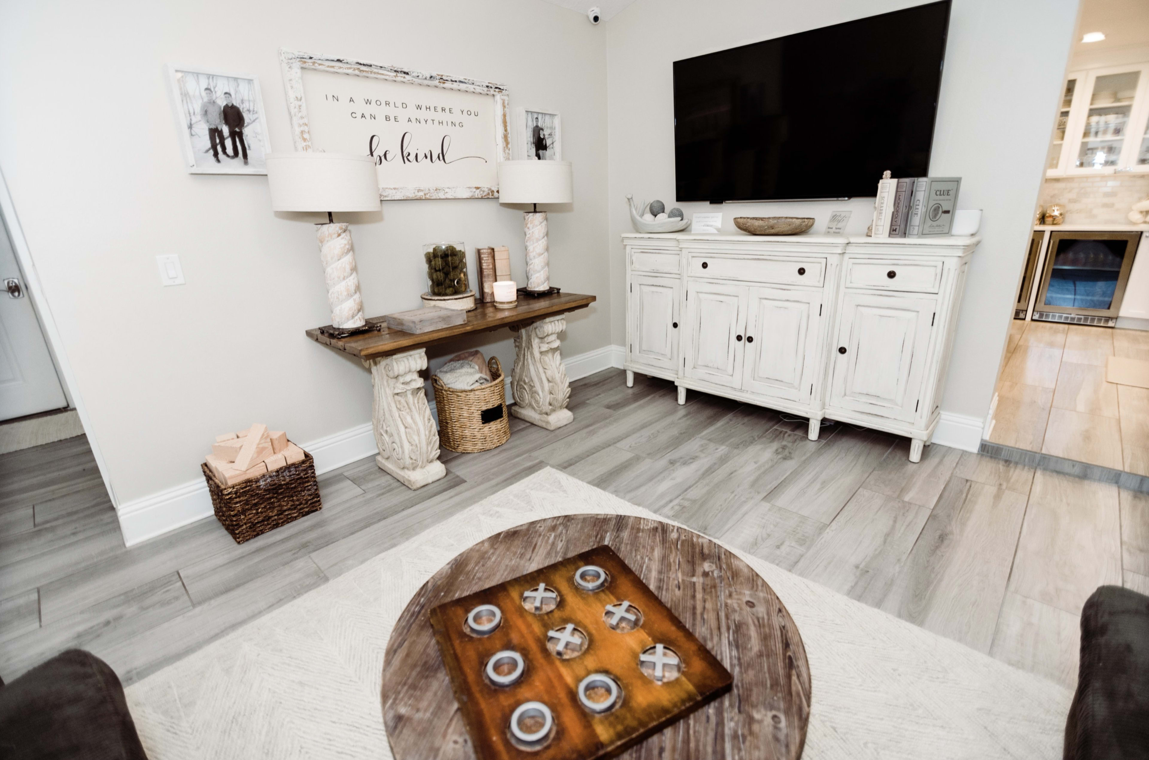 A living room featuring a console table with decorative items, a white cabinet, and a large television mounted on the wall.