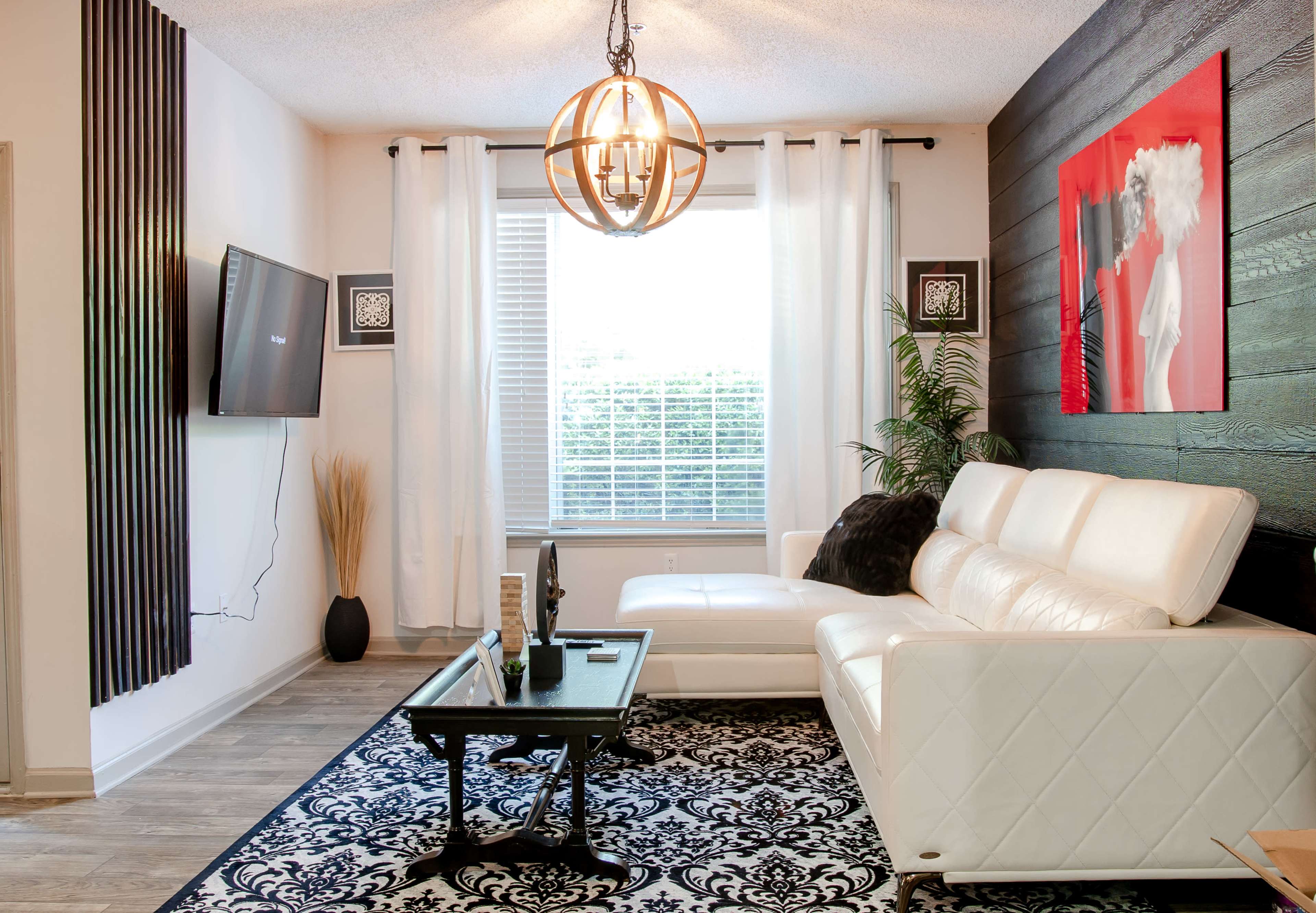 A modern living room features a white sectional sofa, a black coffee table, and a large window with sheer curtains, illuminated by a round pendant light.