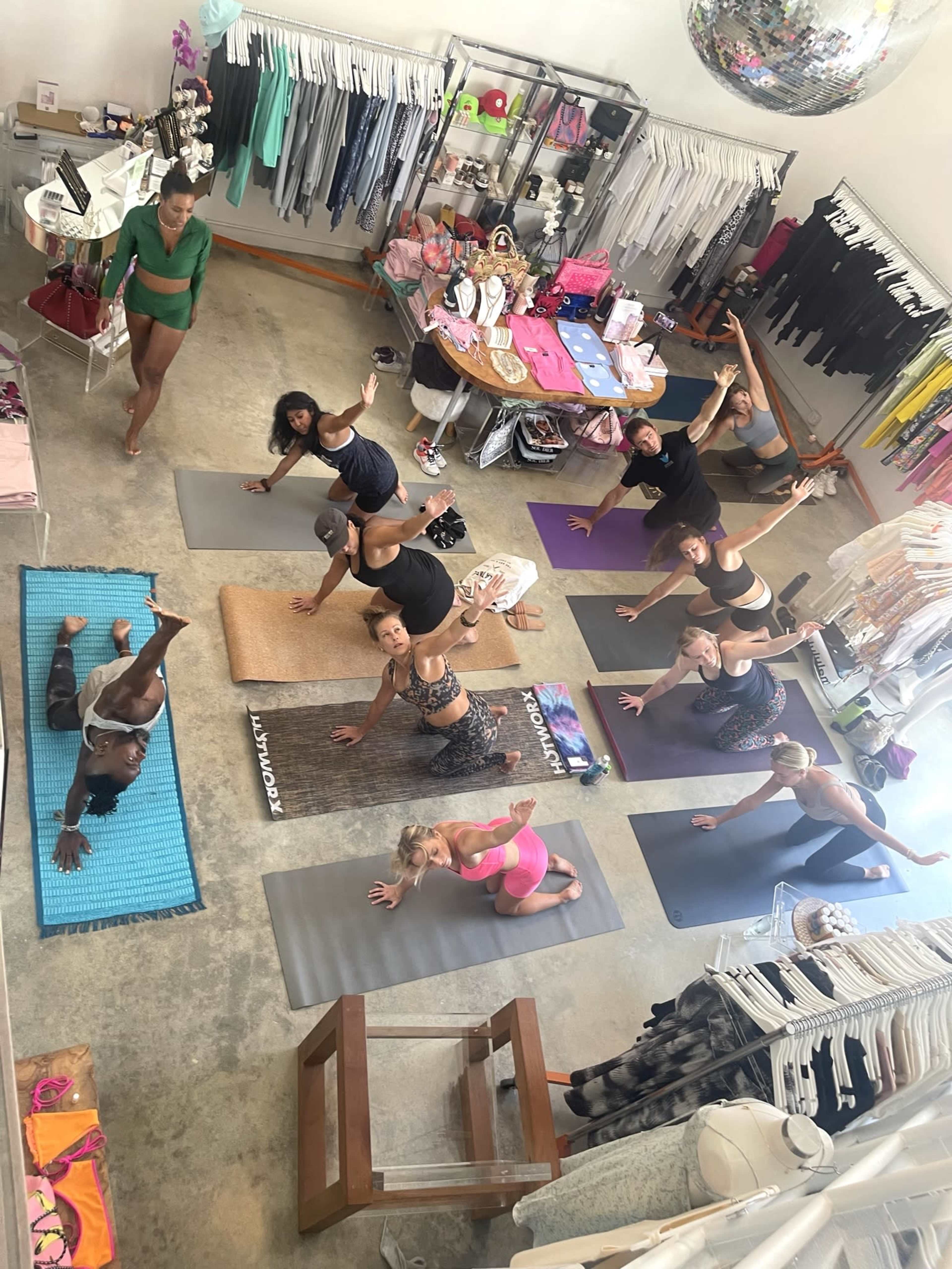 A group of people participate in a yoga class on mats inside a clothing store surrounded by athletic apparel and accessories.