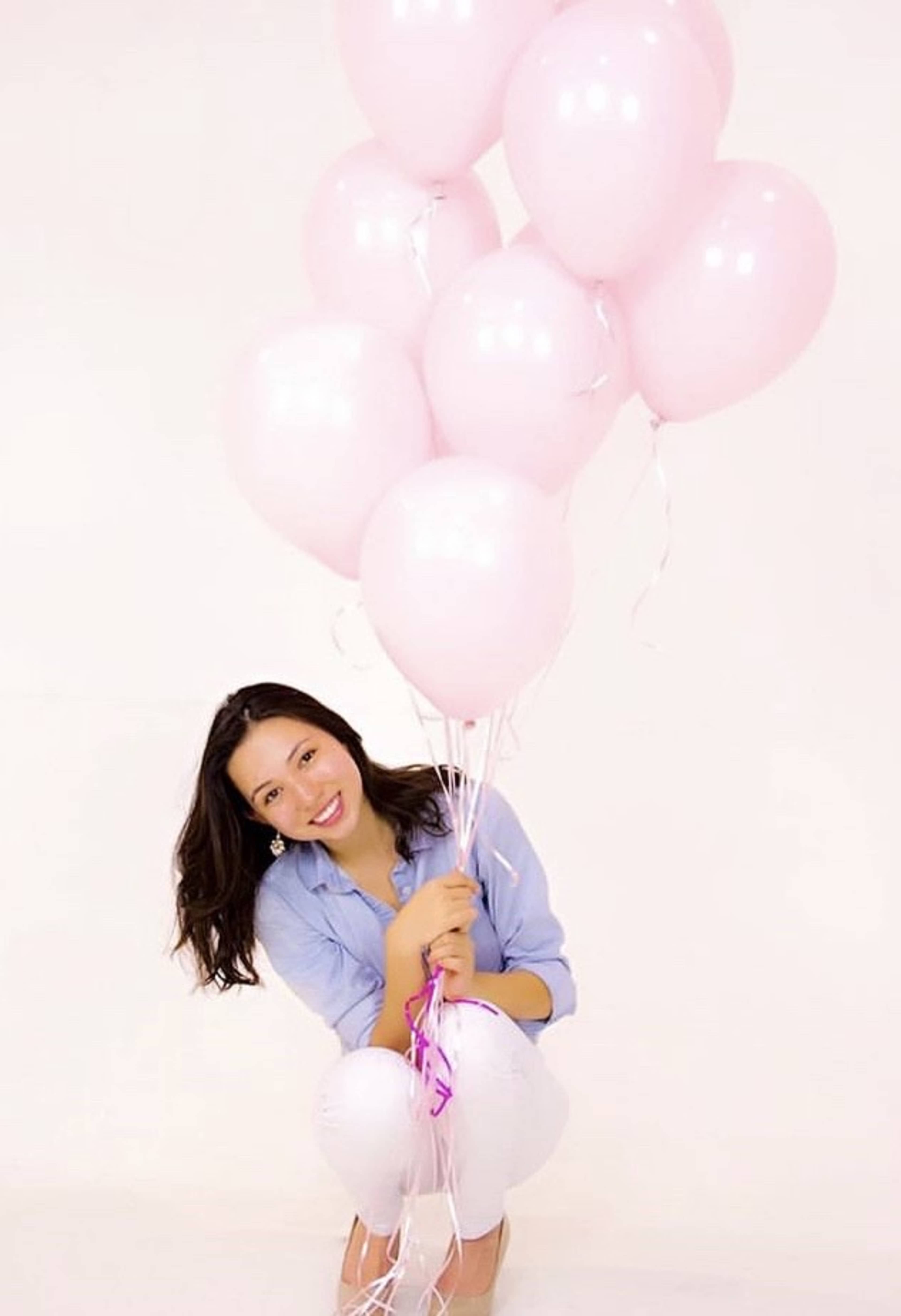 A person kneels while holding a bouquet of pink balloons against a white background.