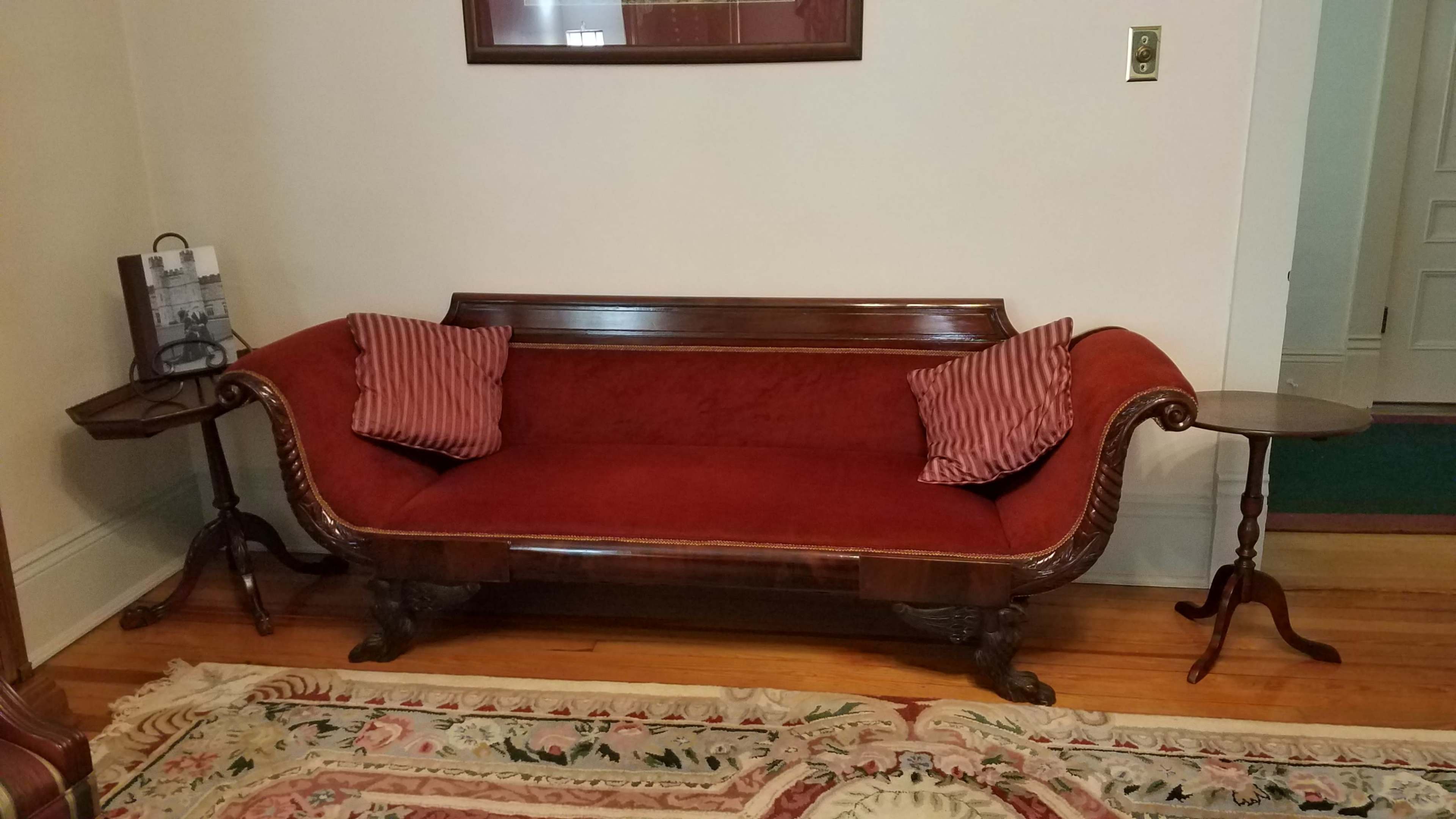 The image shows a red upholstered sofa with striped pillows, positioned next to a small side table on a patterned rug in a room with light-colored walls.