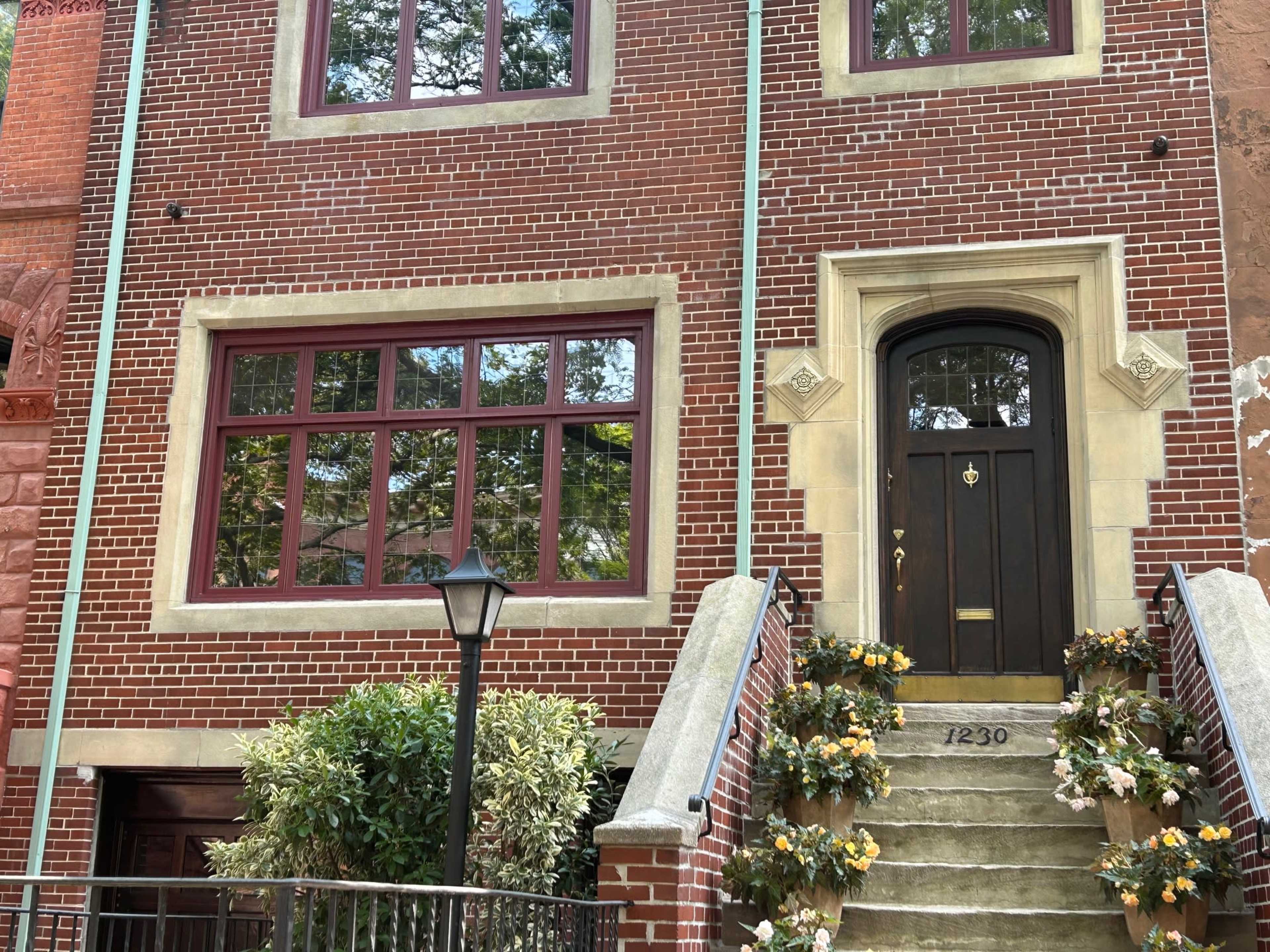A brick building with large windows, a black front door, and a staircase adorned with potted flowers.