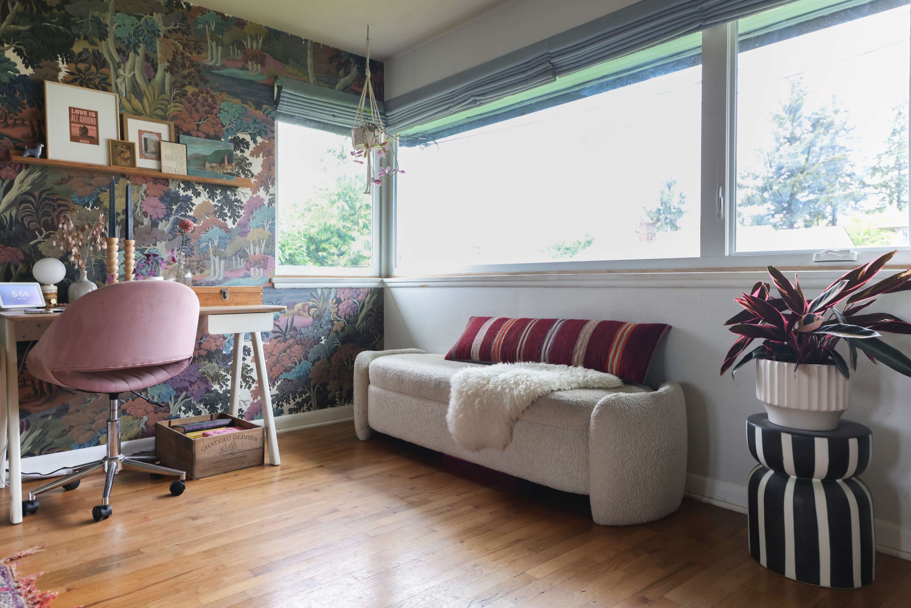 A brightly lit room features a desk with a pink chair, a cozy sofa adorned with striped cushions, and a colorful wall mural.
