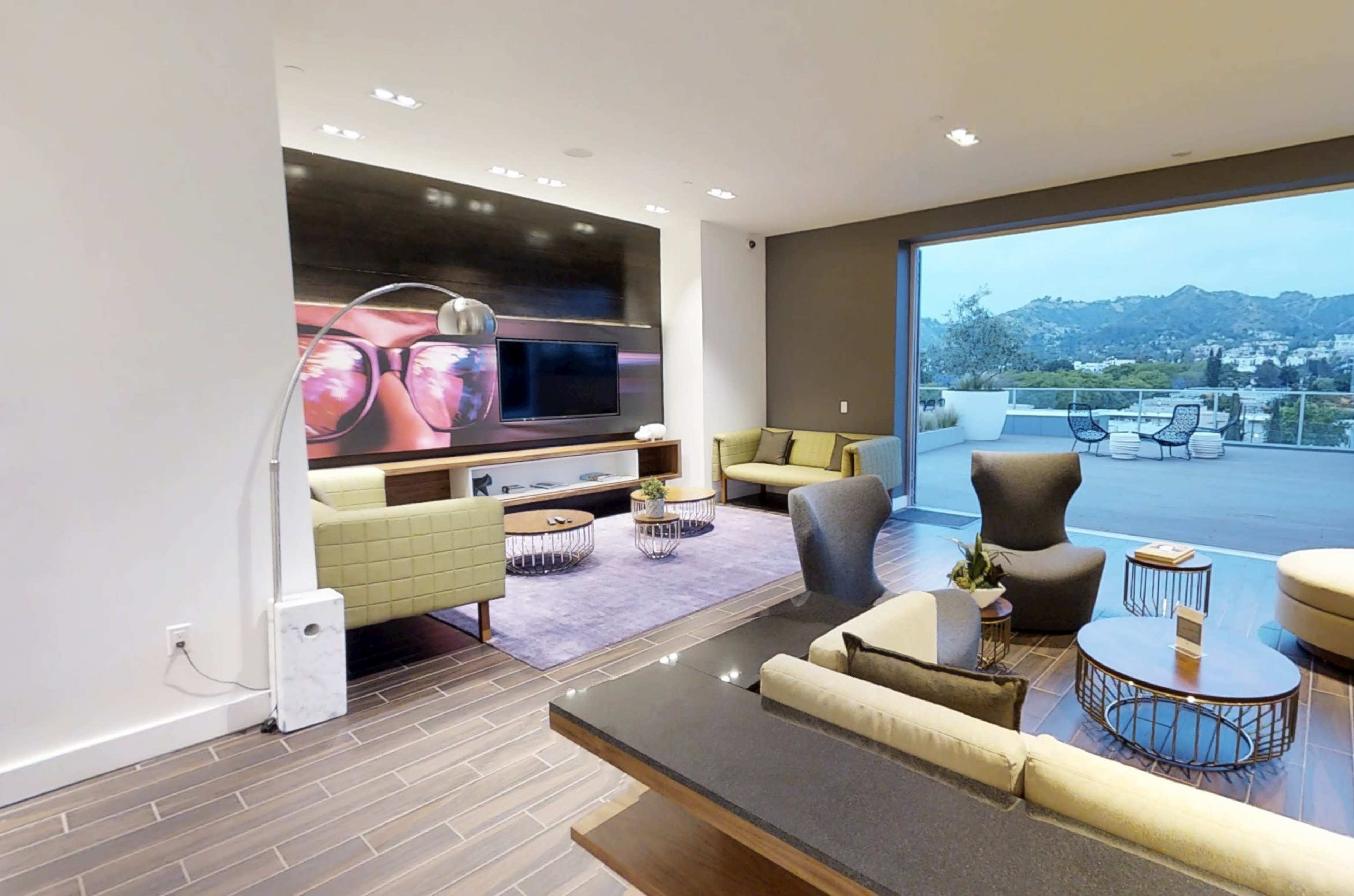 The image shows a modern living room with contemporary furniture, large windows, and a view of mountains in the background.