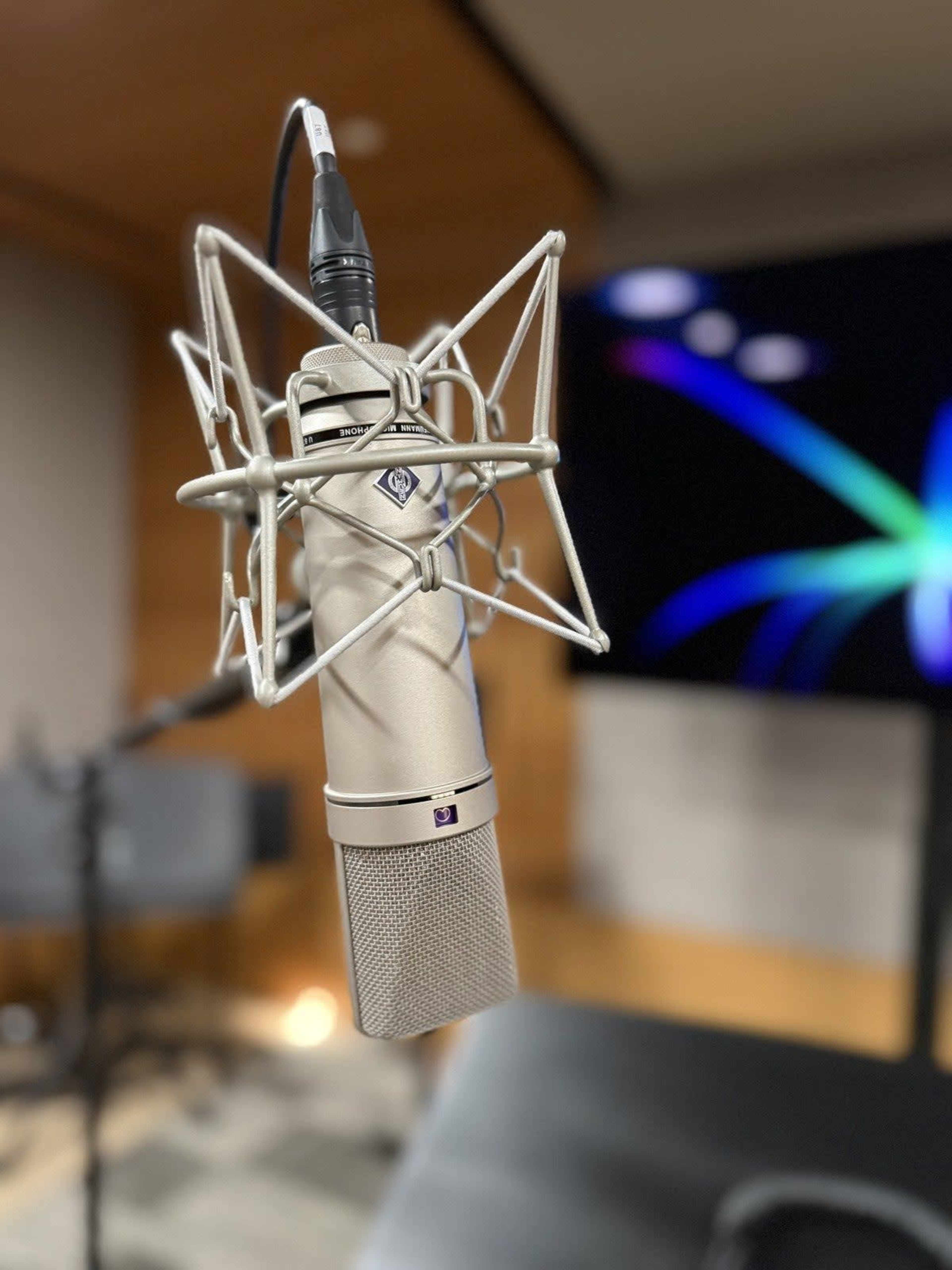 A professional microphone is positioned on a stand in a sound studio, with a colorful digital display in the background.