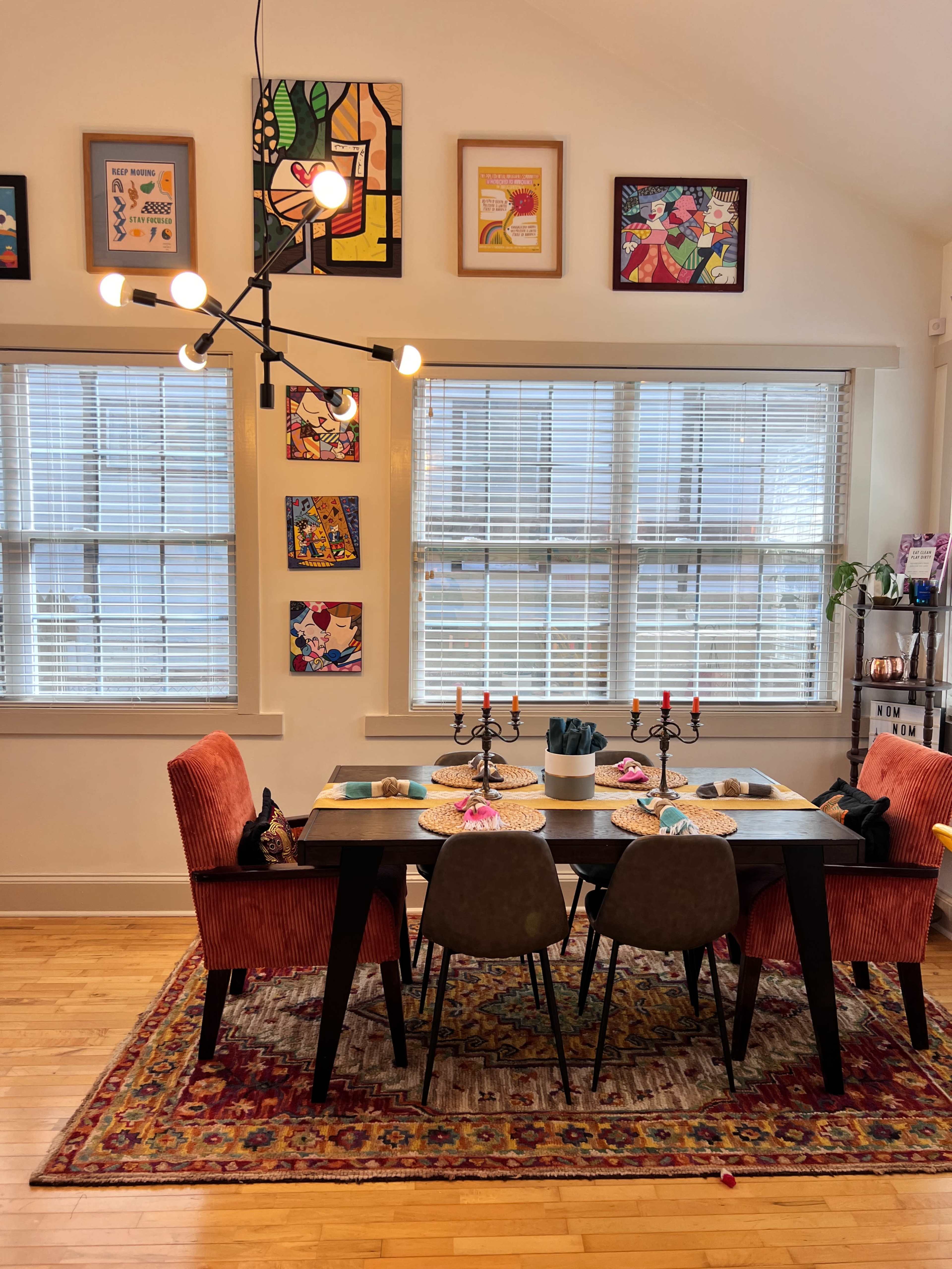 A dining area features a table set with decorative plates and candles, surrounded by colorful chairs and adorned with framed artwork on the walls.