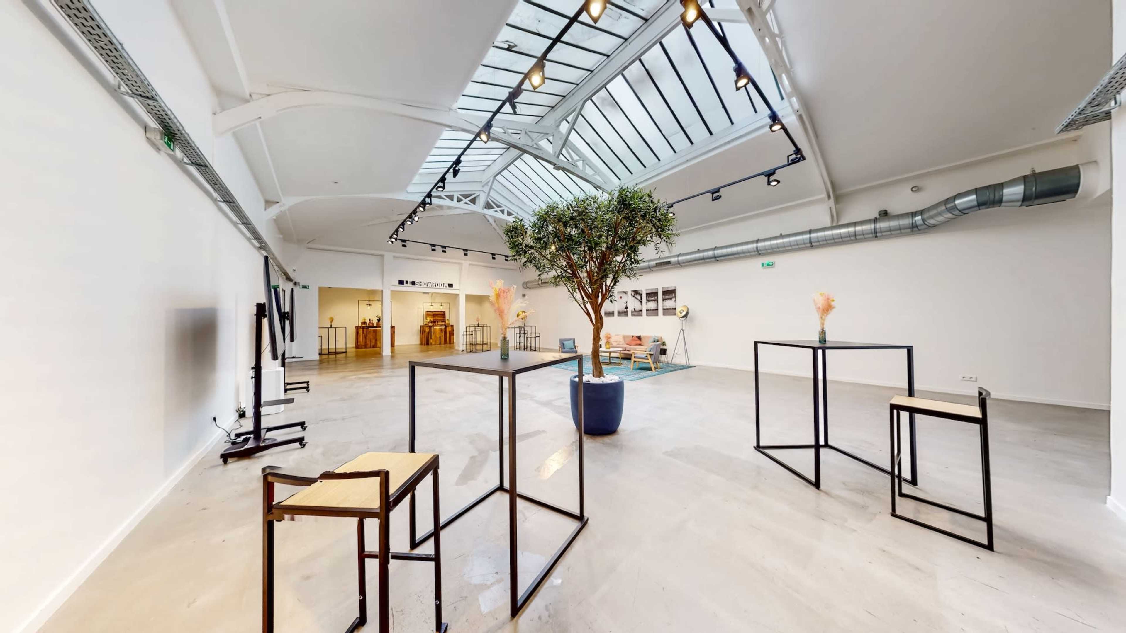 The image shows a spacious, well-lit interior with modern displays and greenery, featuring black and wooden furniture.
