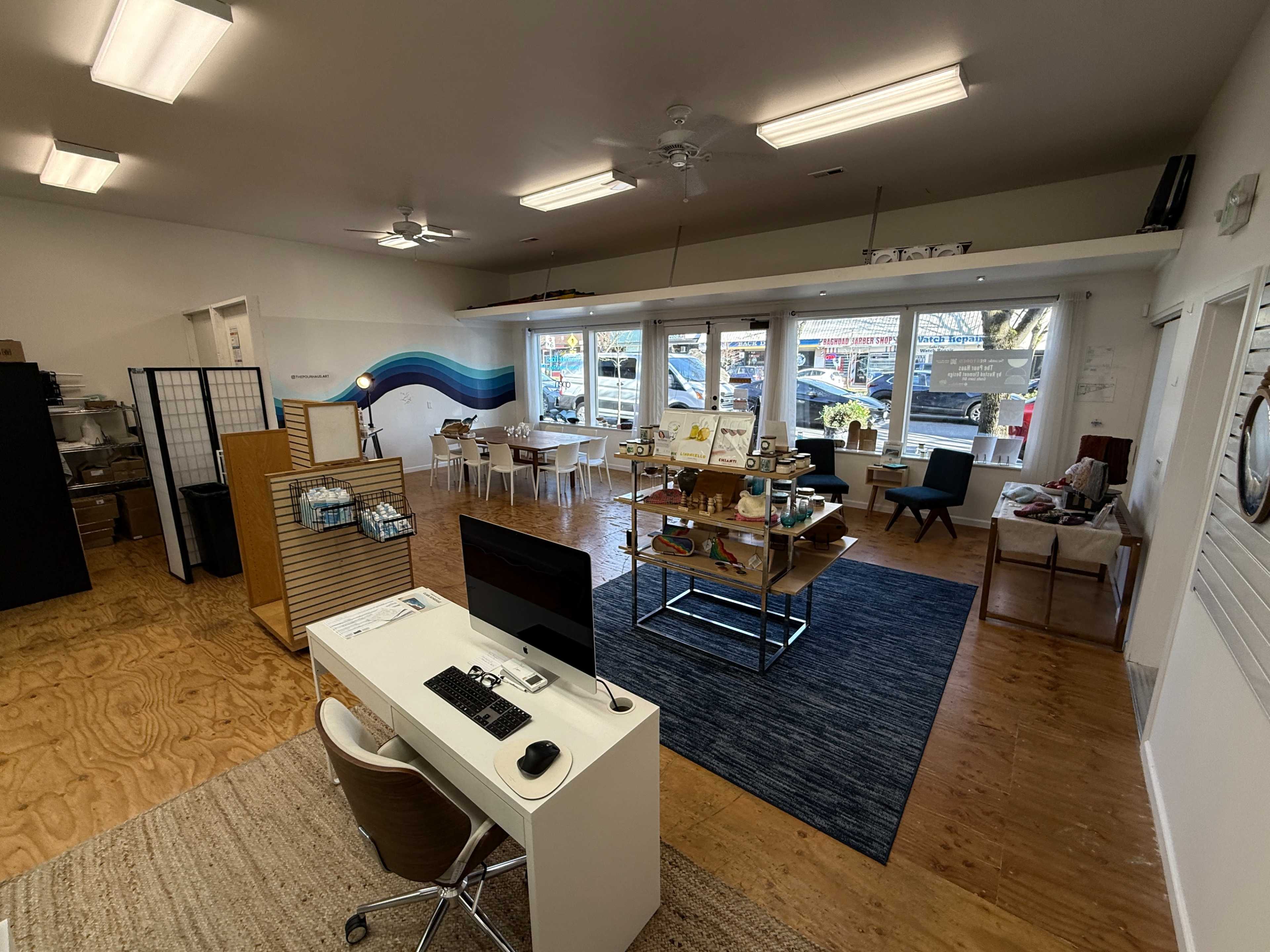 The image depicts a spacious, well-lit interior of a modern retail or office space with tables, chairs, and a reception area.