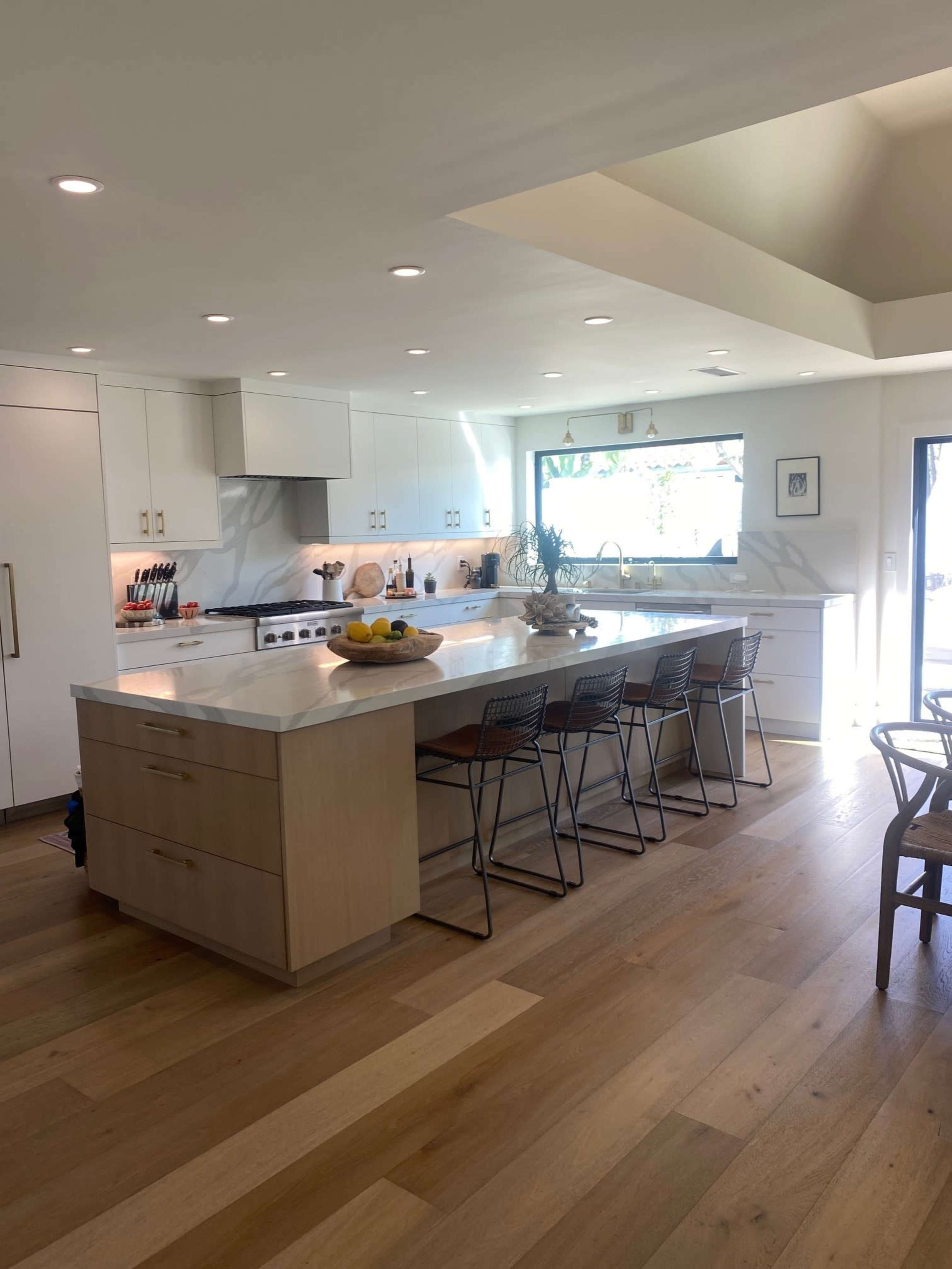 A modern kitchen with white cabinetry, a central island with seating, and large windows that allow natural light in.