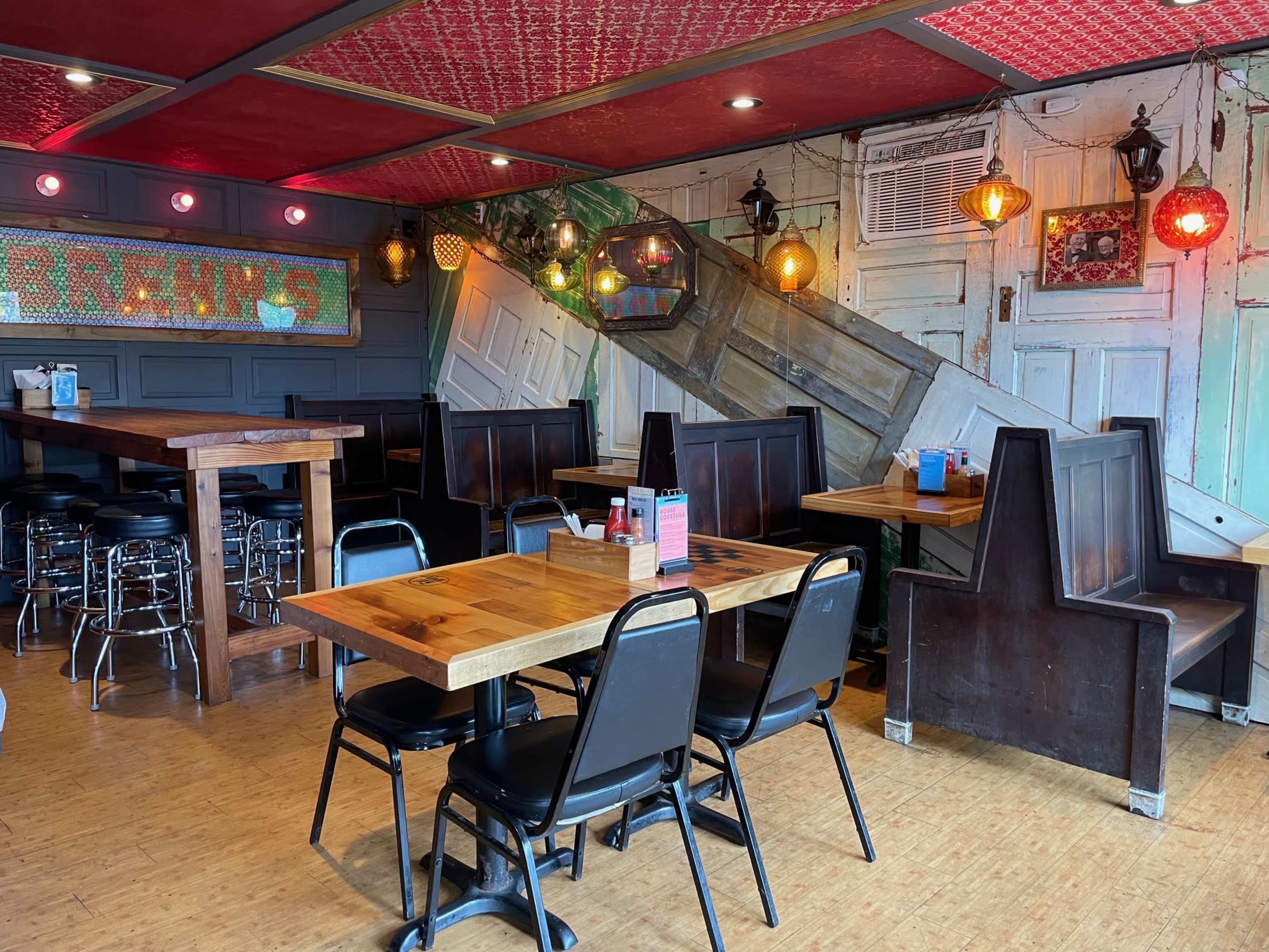 The image shows a restaurant interior with wooden tables and black chairs, featuring a mix of rustic decor and colorful lighting elements.