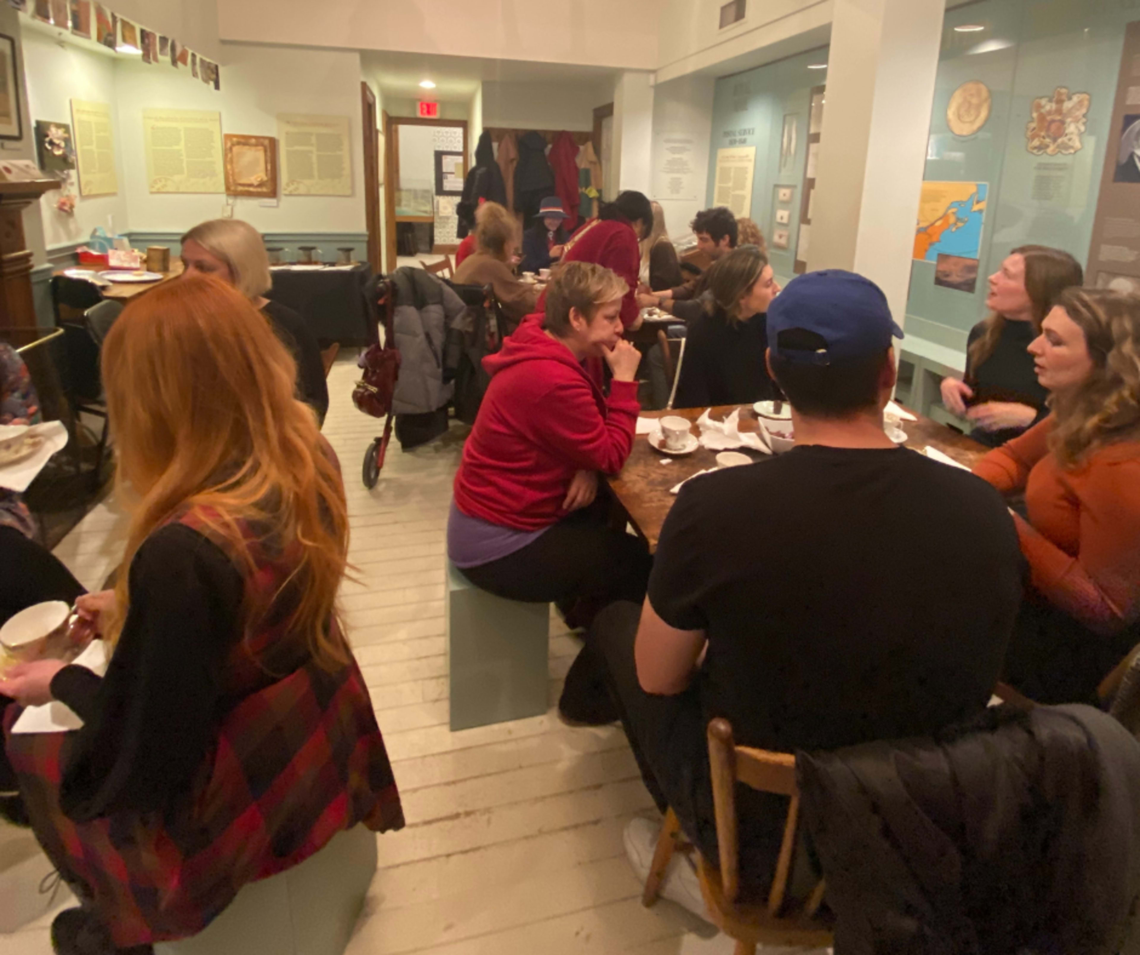A group of people is gathered around tables in a cafe-like space, engaging in conversation while some are enjoying bowls of food.