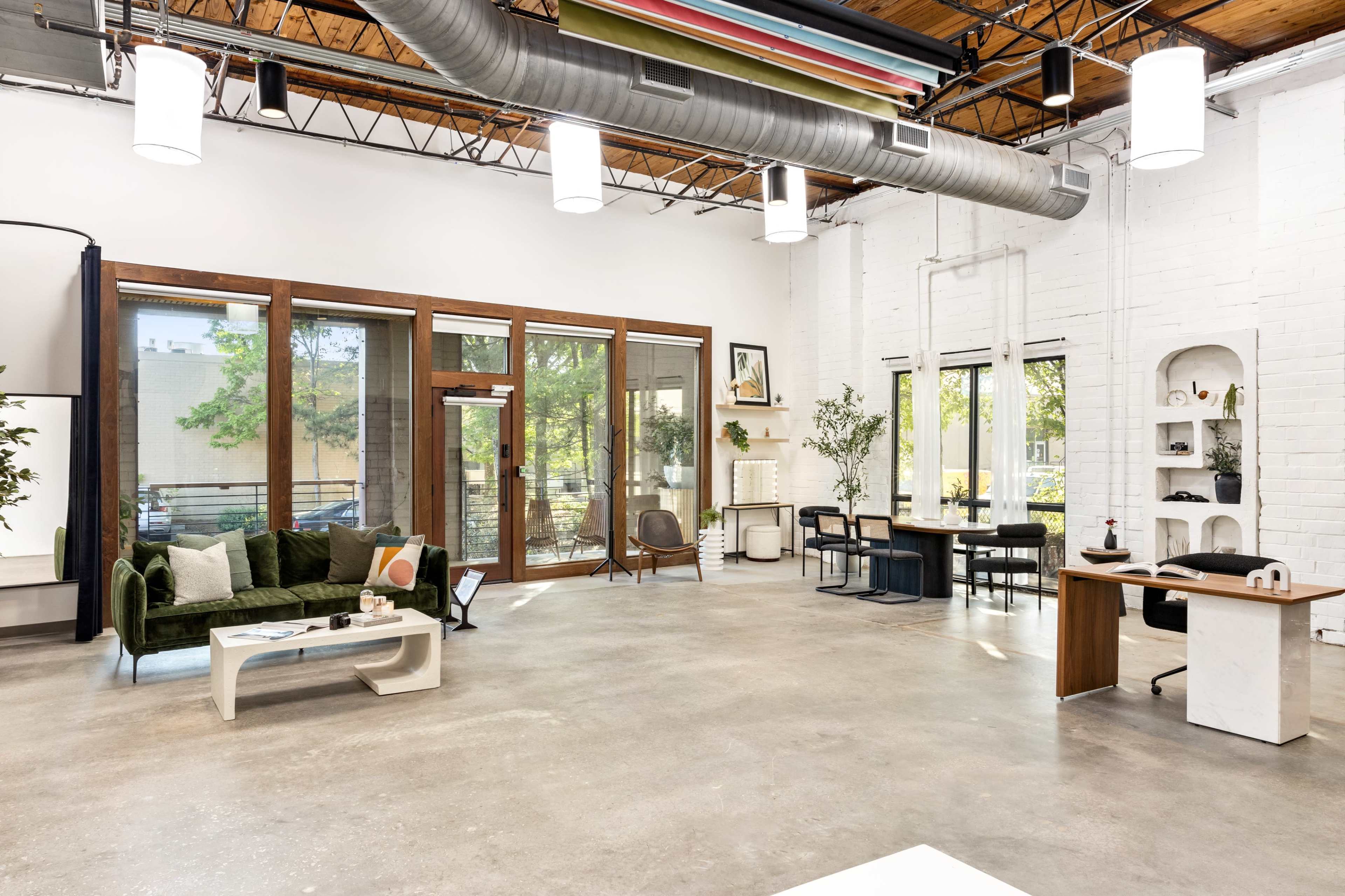 A modern interior space with a green sofa, wooden furniture, large windows, and concrete flooring.
