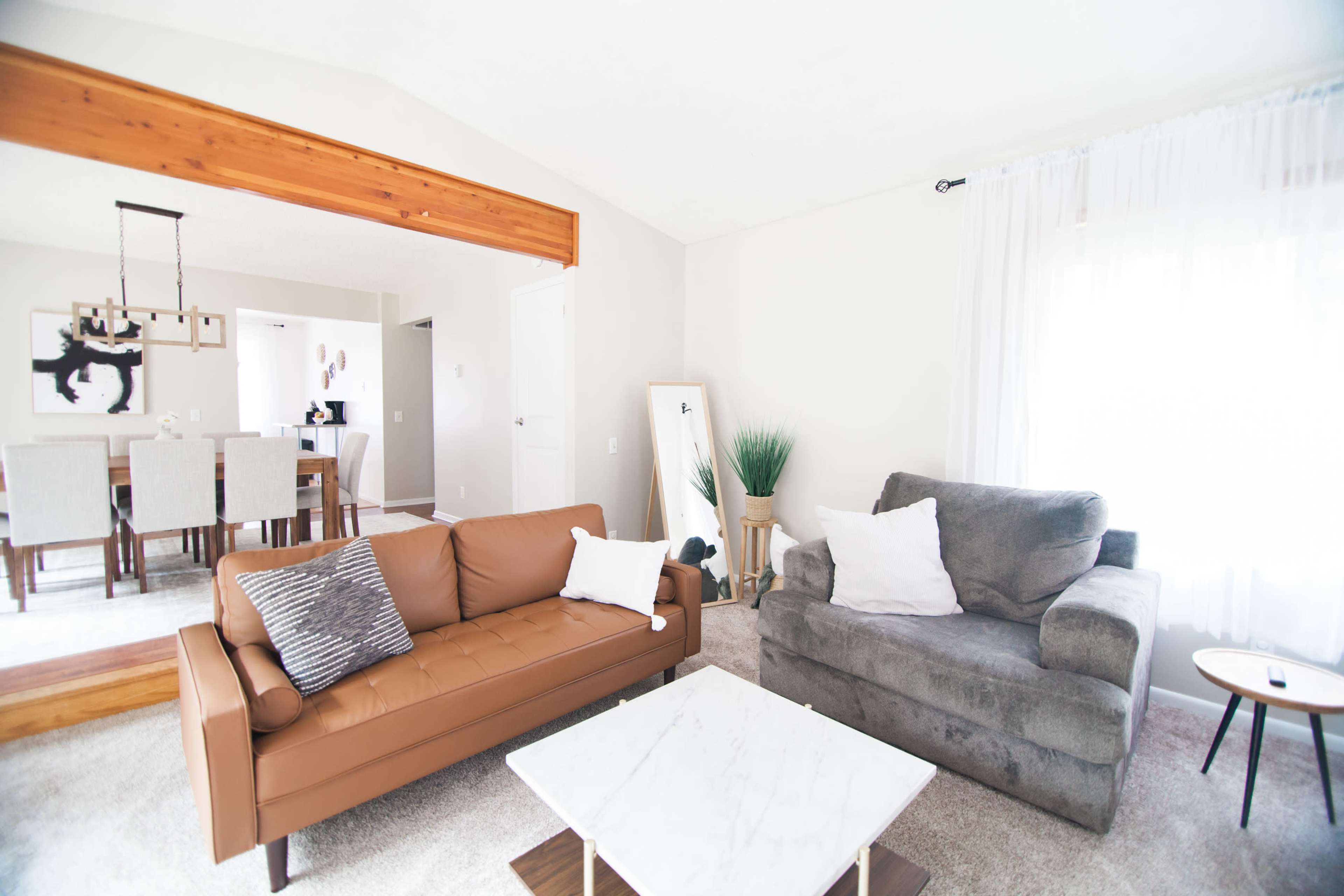 A living room featuring a brown leather sofa, a gray armchair, a marble-top coffee table, and a dining area visible in the mirror.