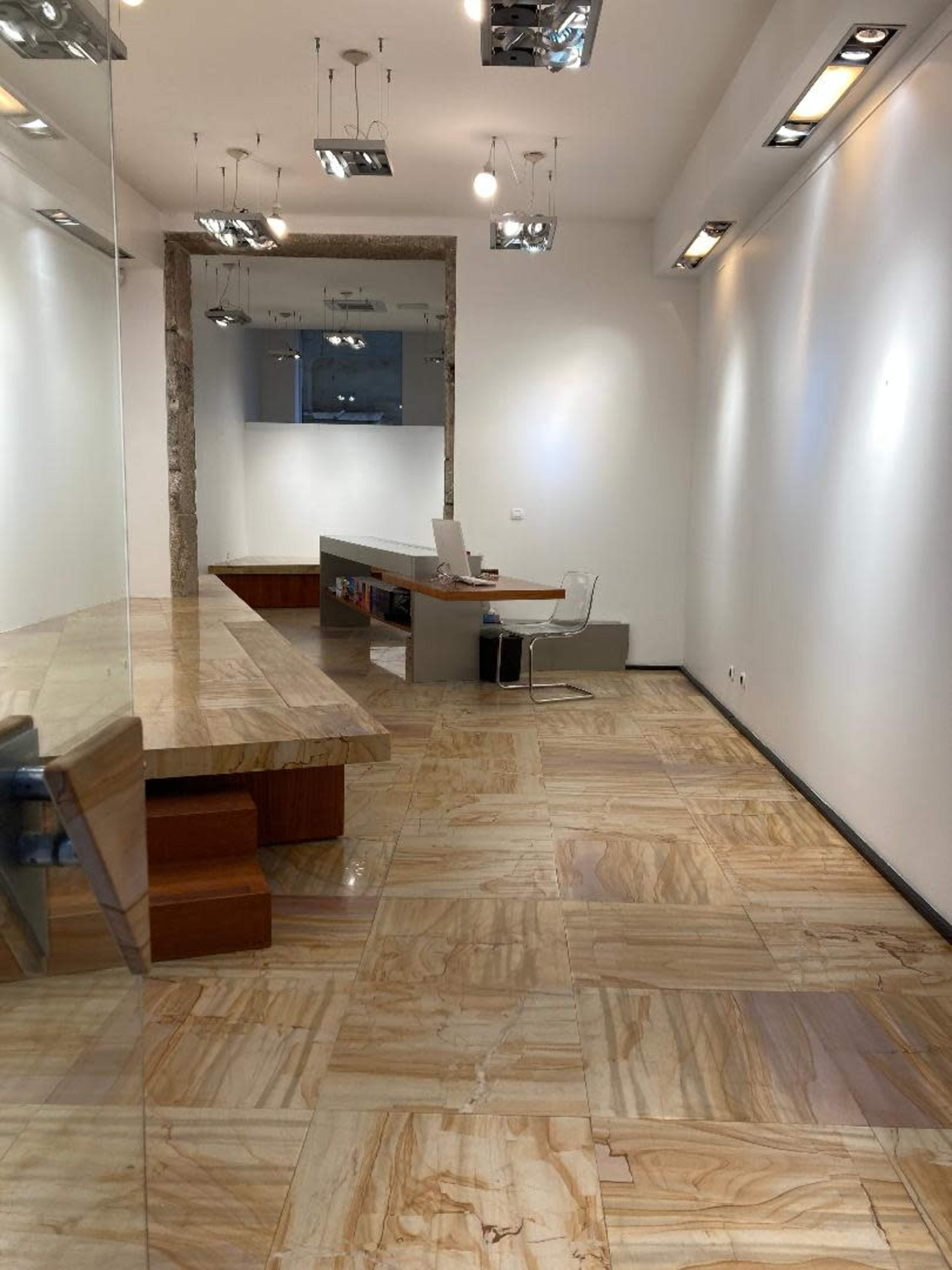 The image shows a minimalist office space featuring a polished stone floor, a modern desk with a chair, and bright lighting.