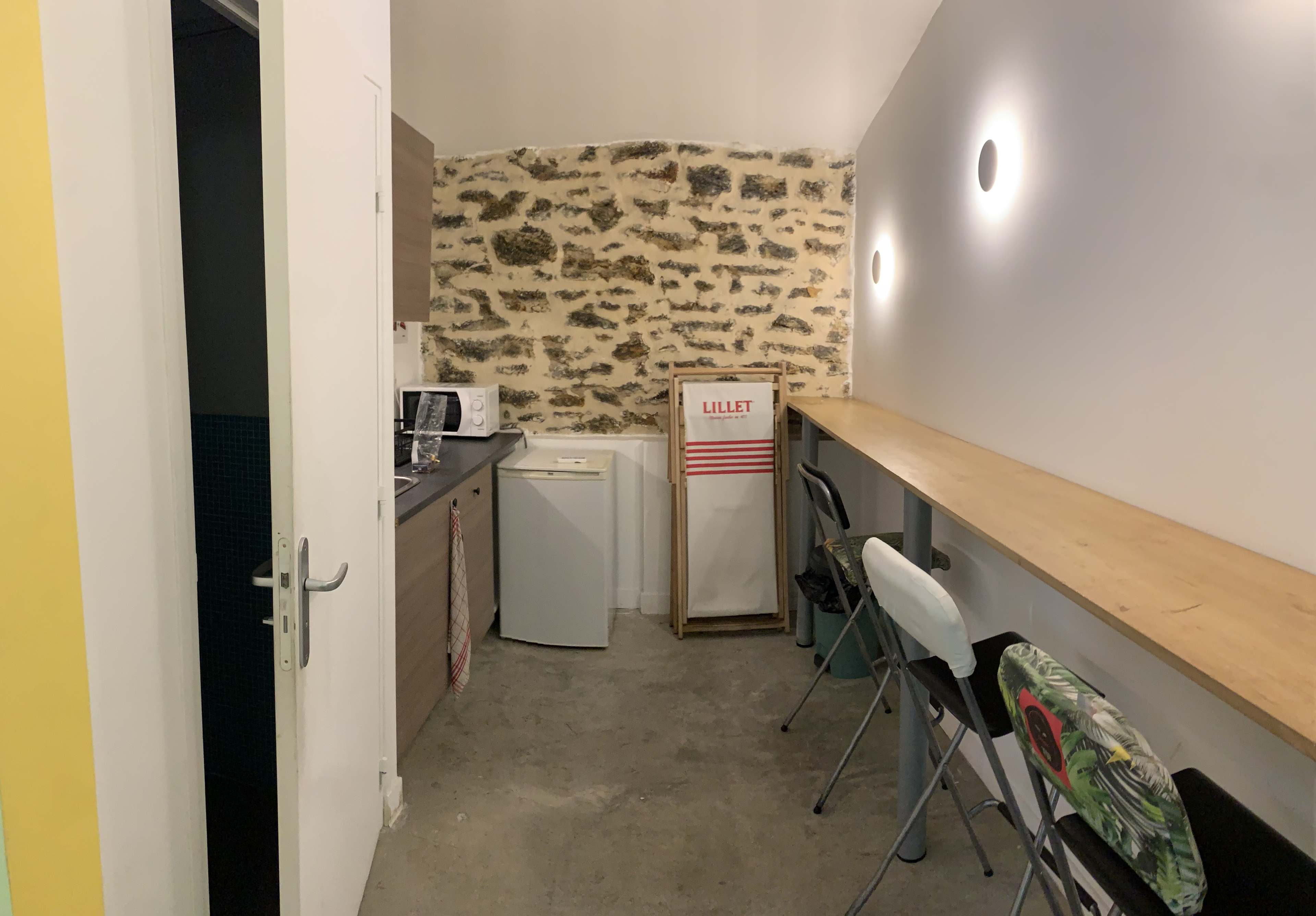 A small kitchen area with a microwave, refrigerator, and a long wooden counter with several stools.